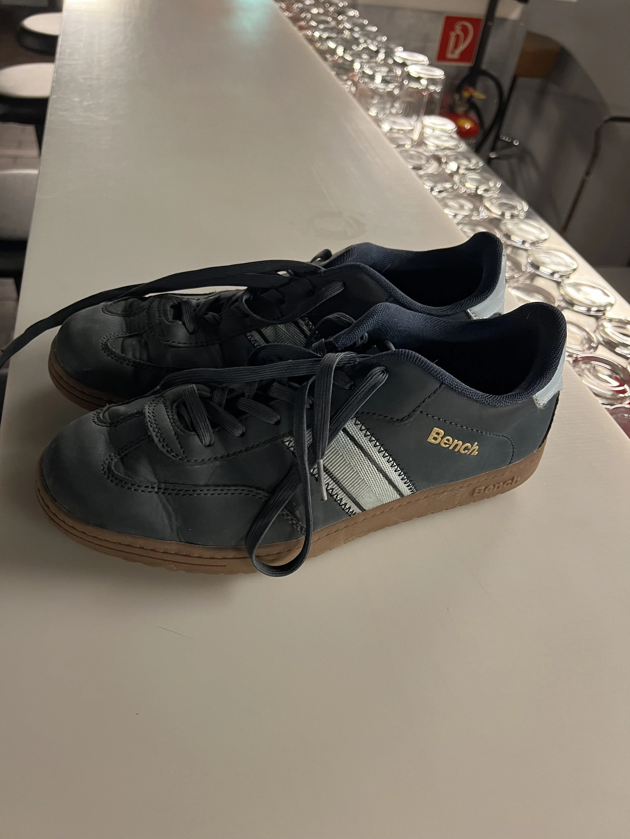 Schwarze Turnschuhe mit brauner Sohle, auf einem weißen Tisch.