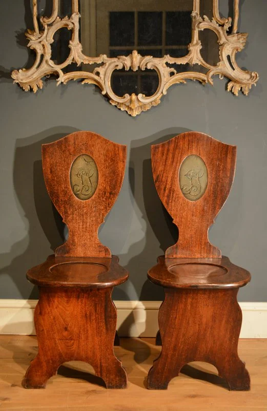 A pair of George II mahogany hall chairs, the shield shaped backs having a recessed painted oval with the initials 'JS'