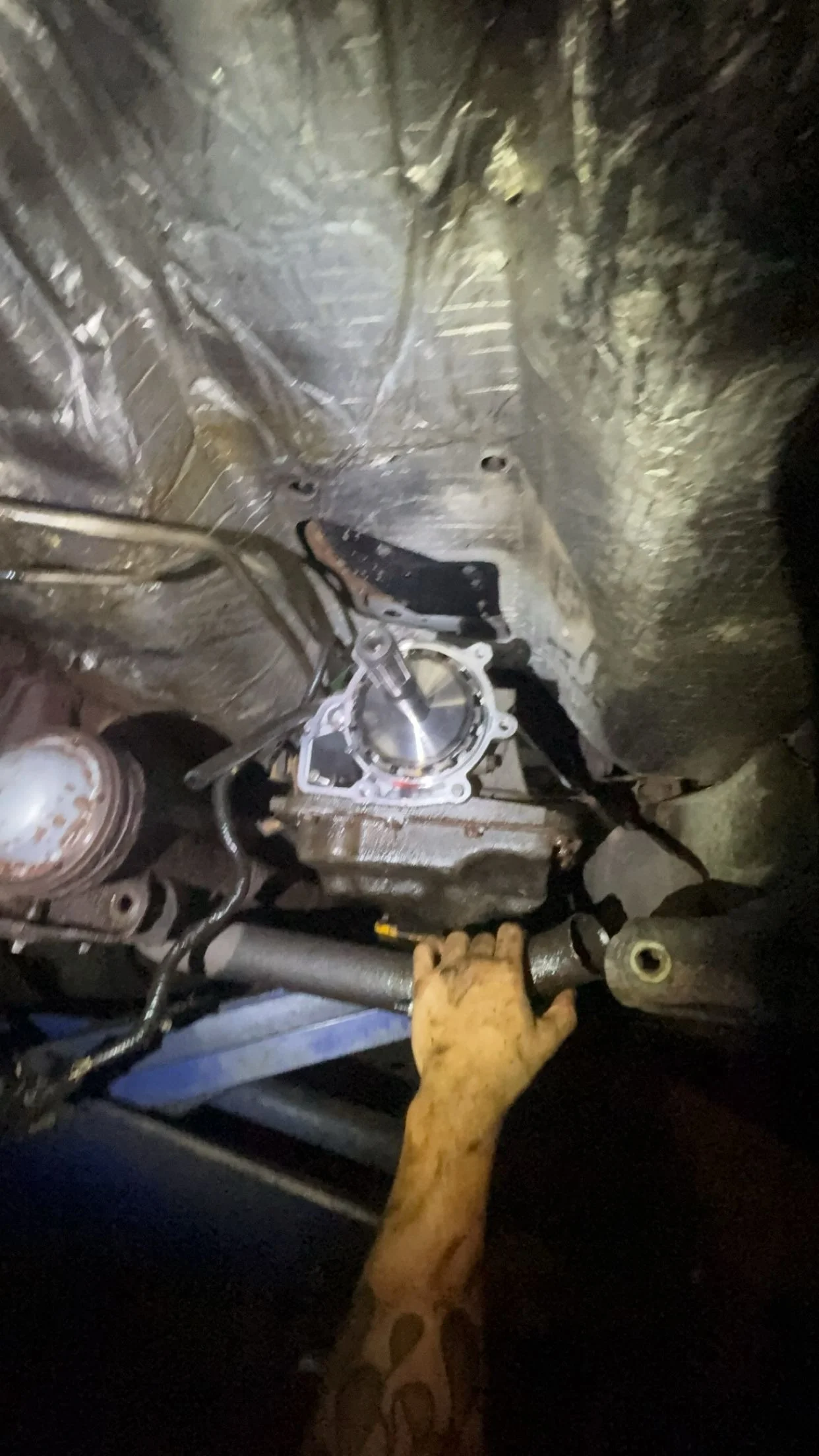 A person wearing a glove working on a mechanical component in a confined space, with tools and machinery parts visible around.