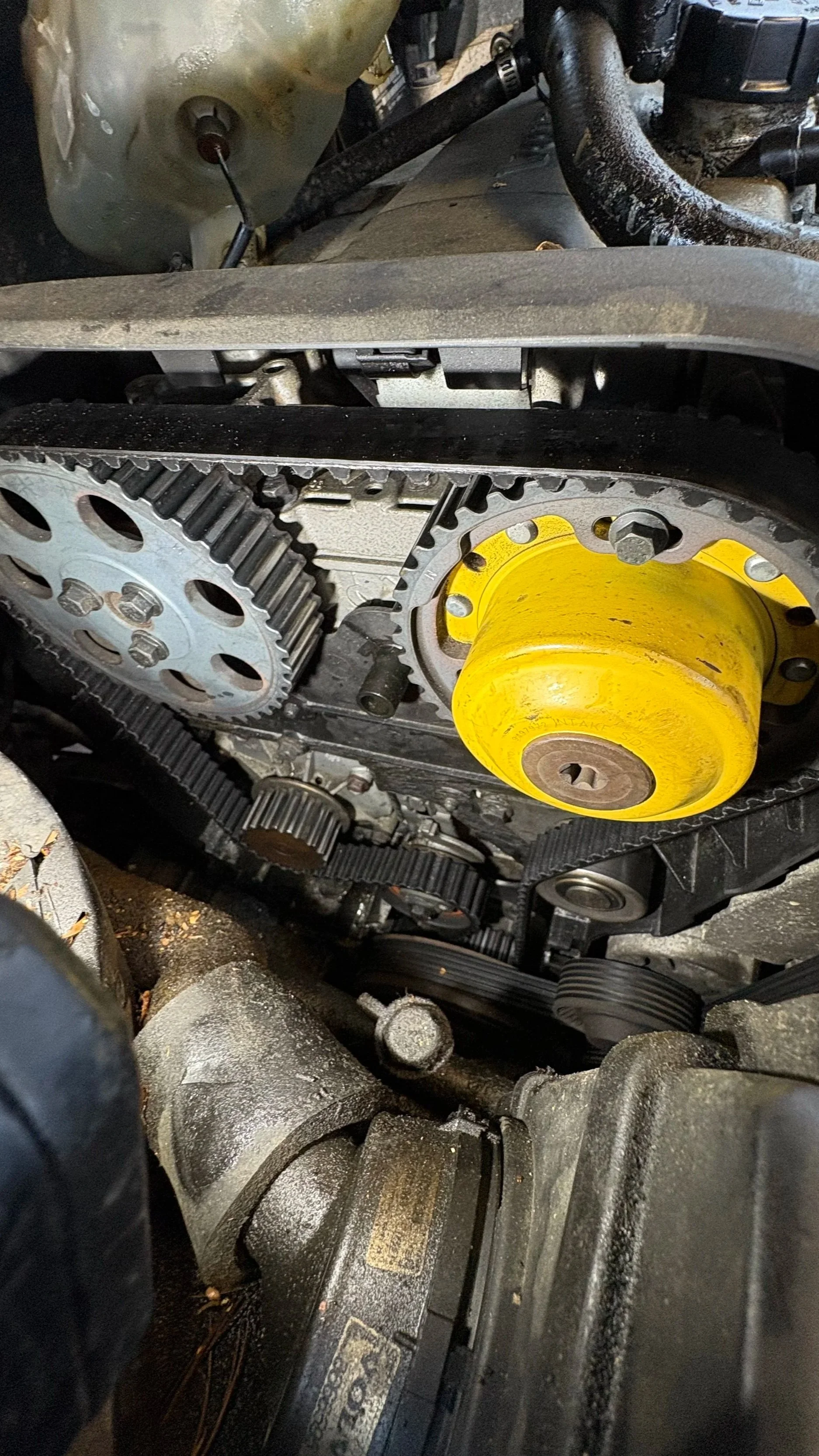 Close-up view of a vehicle engine's timing belt, gears, and a yellow component.