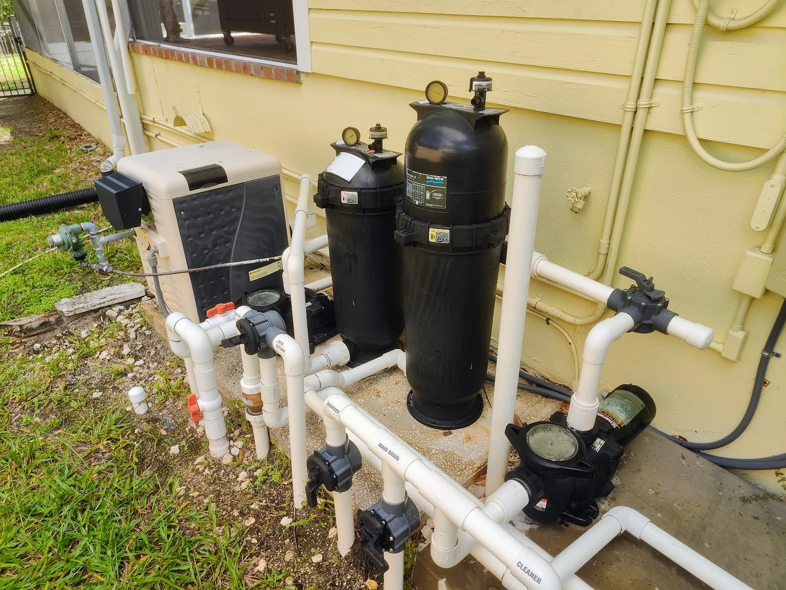 Outdoor pool equipment with filters, pumps, and plumbing, and a gas heater installed next to the house exterior wall.