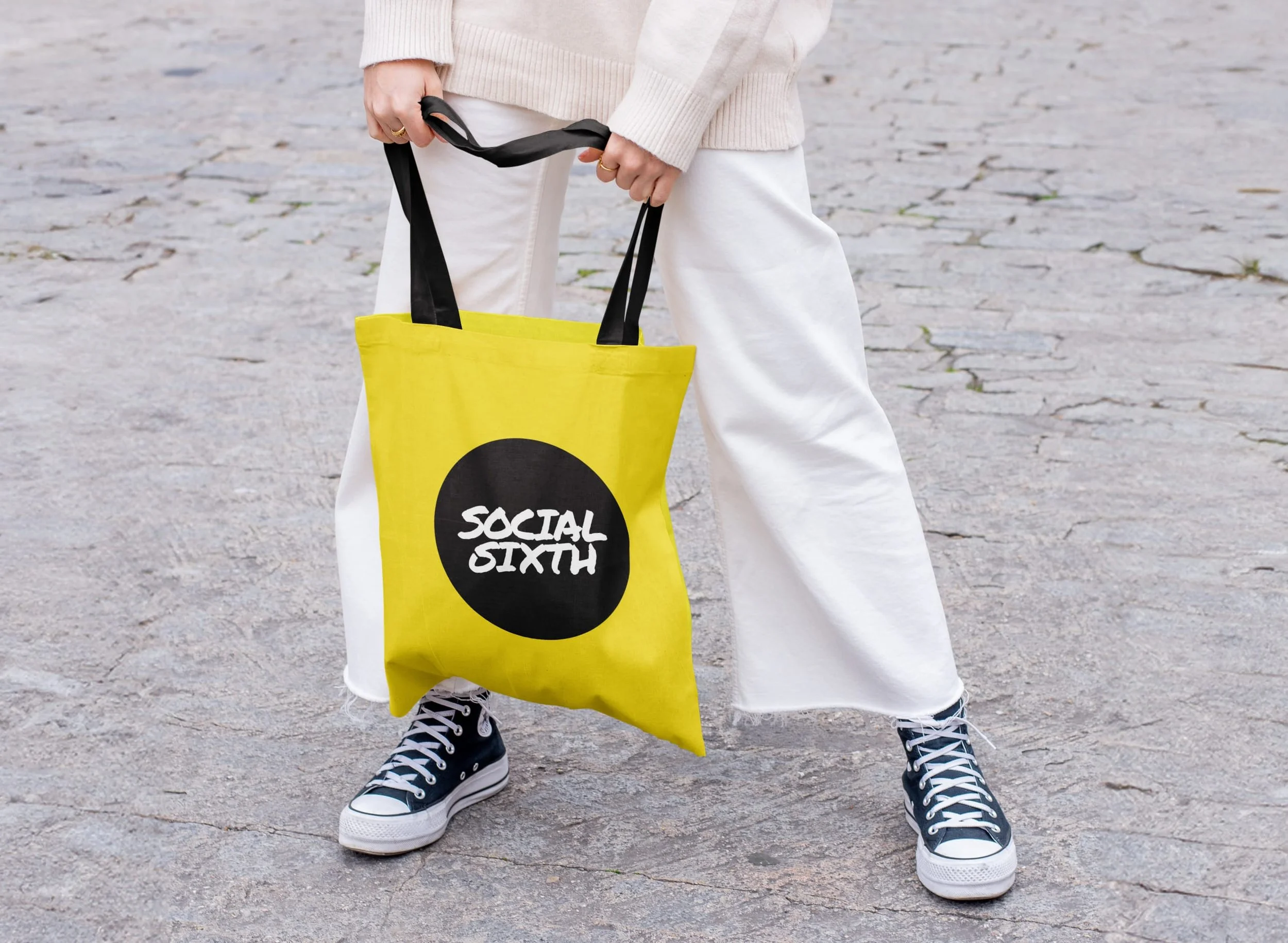 A woman in cream and white holding a yellow Social Sixth branded tote bag with black handles