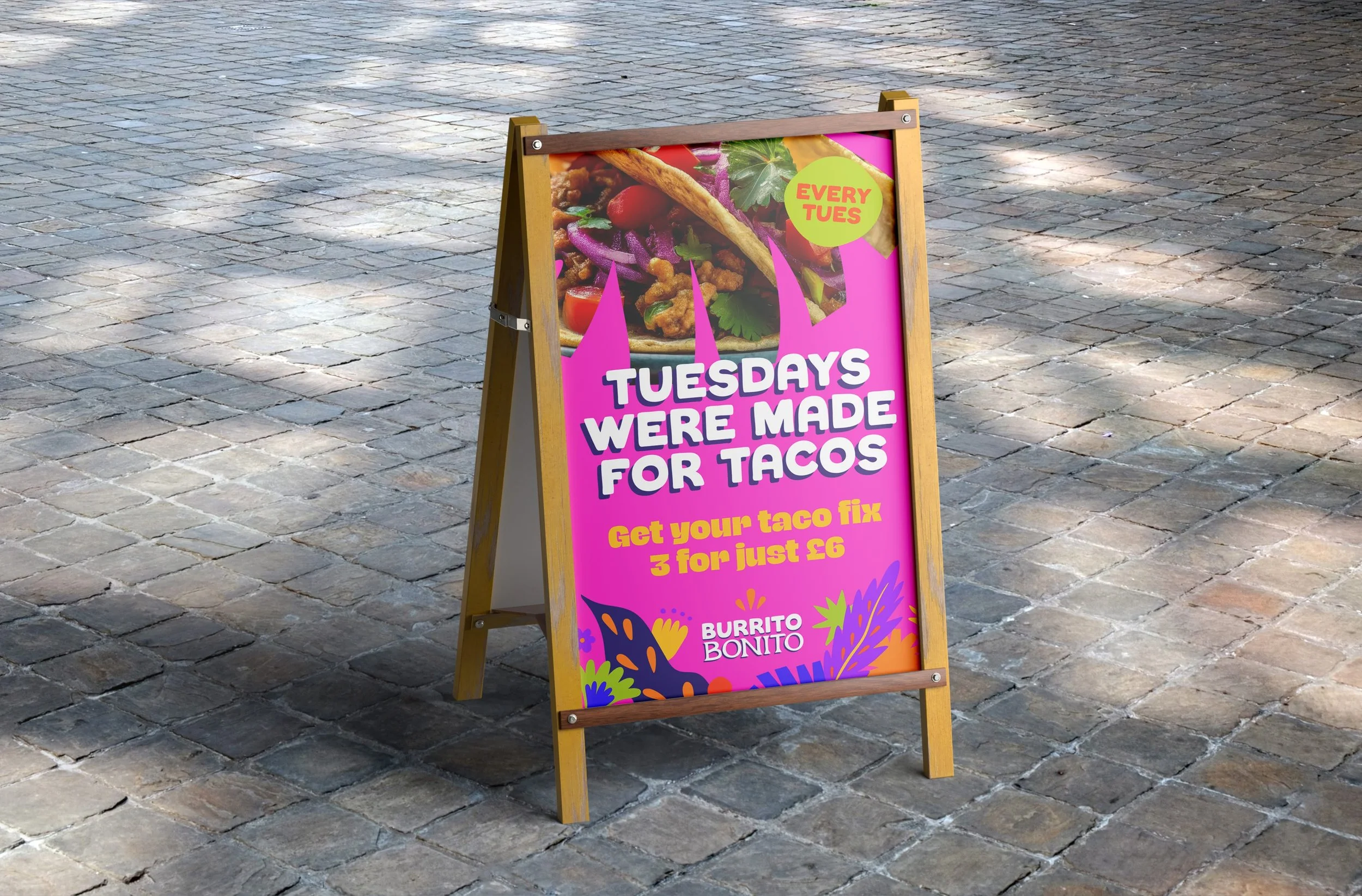 A colourful pavement sign advertising tacos at Burrito Bonito, mentioning a special deal every Tuesday.