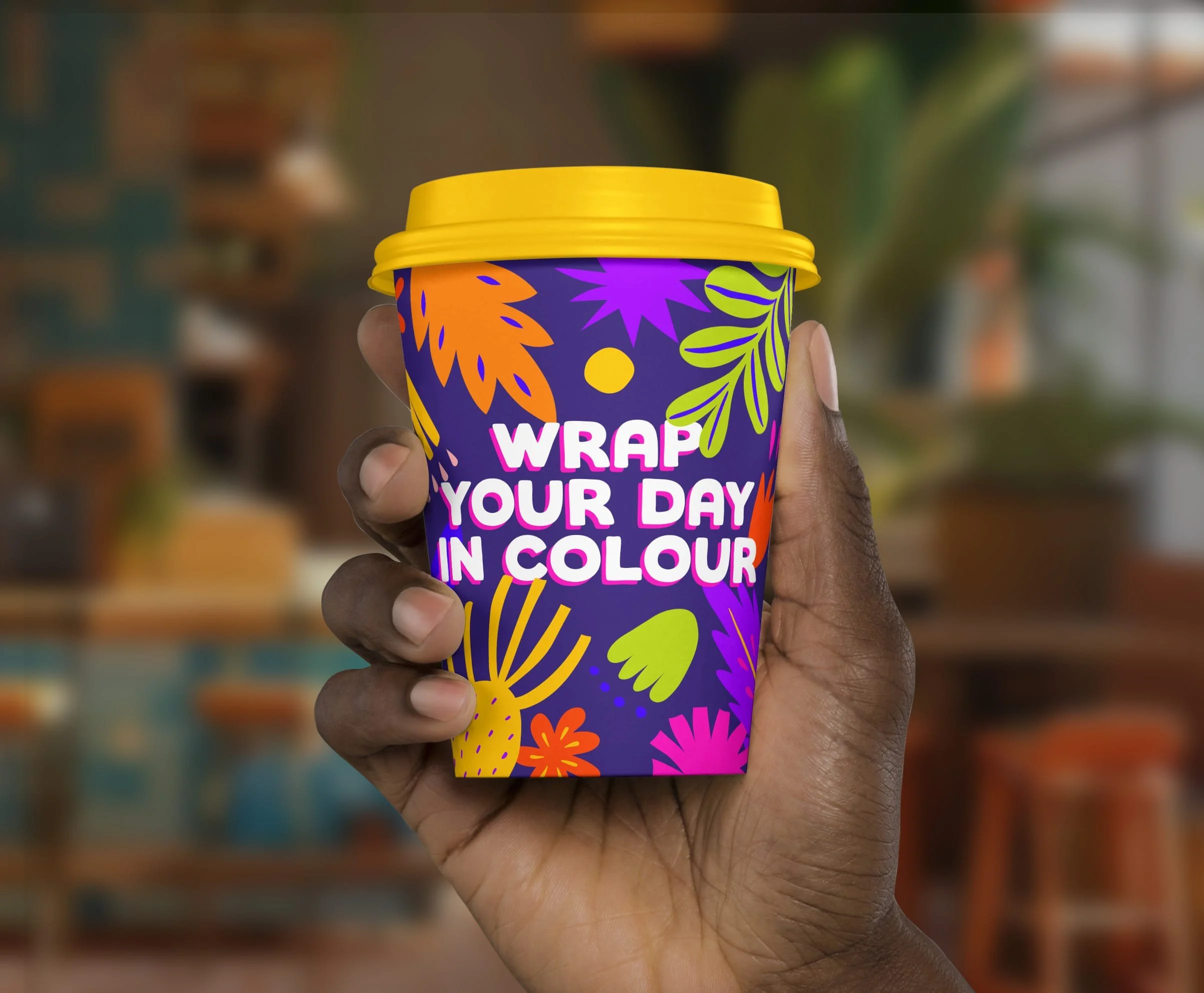 A man holding a Burrito Bonito branded coffee cup with a yellow lid and the words Wrap your day in colour in the front