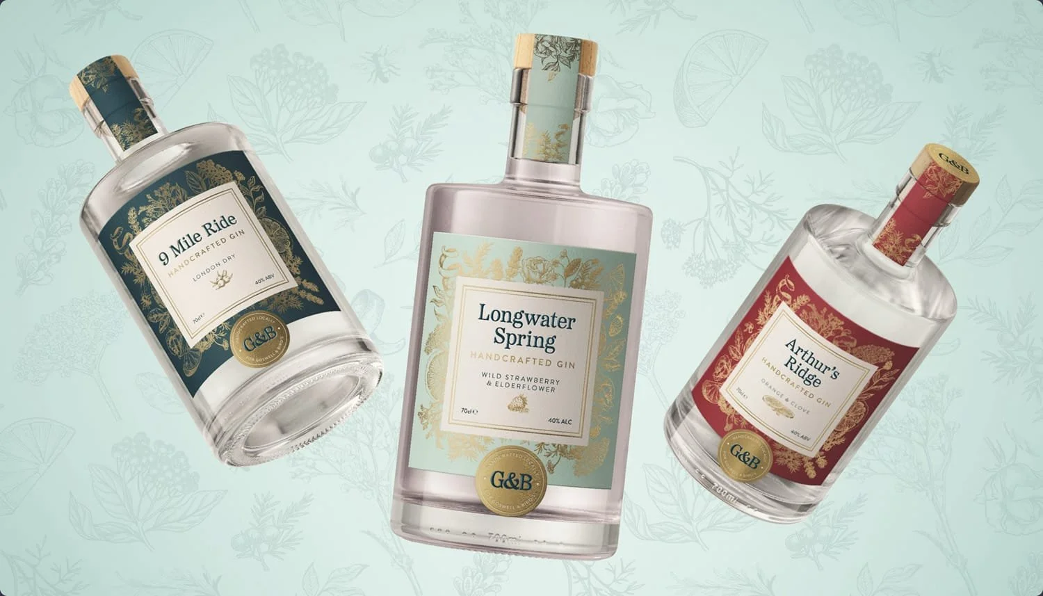 Three bottles of G&B handcrafted gin with floral labels, floating against a light blue background with faint floral and citrus illustrations.