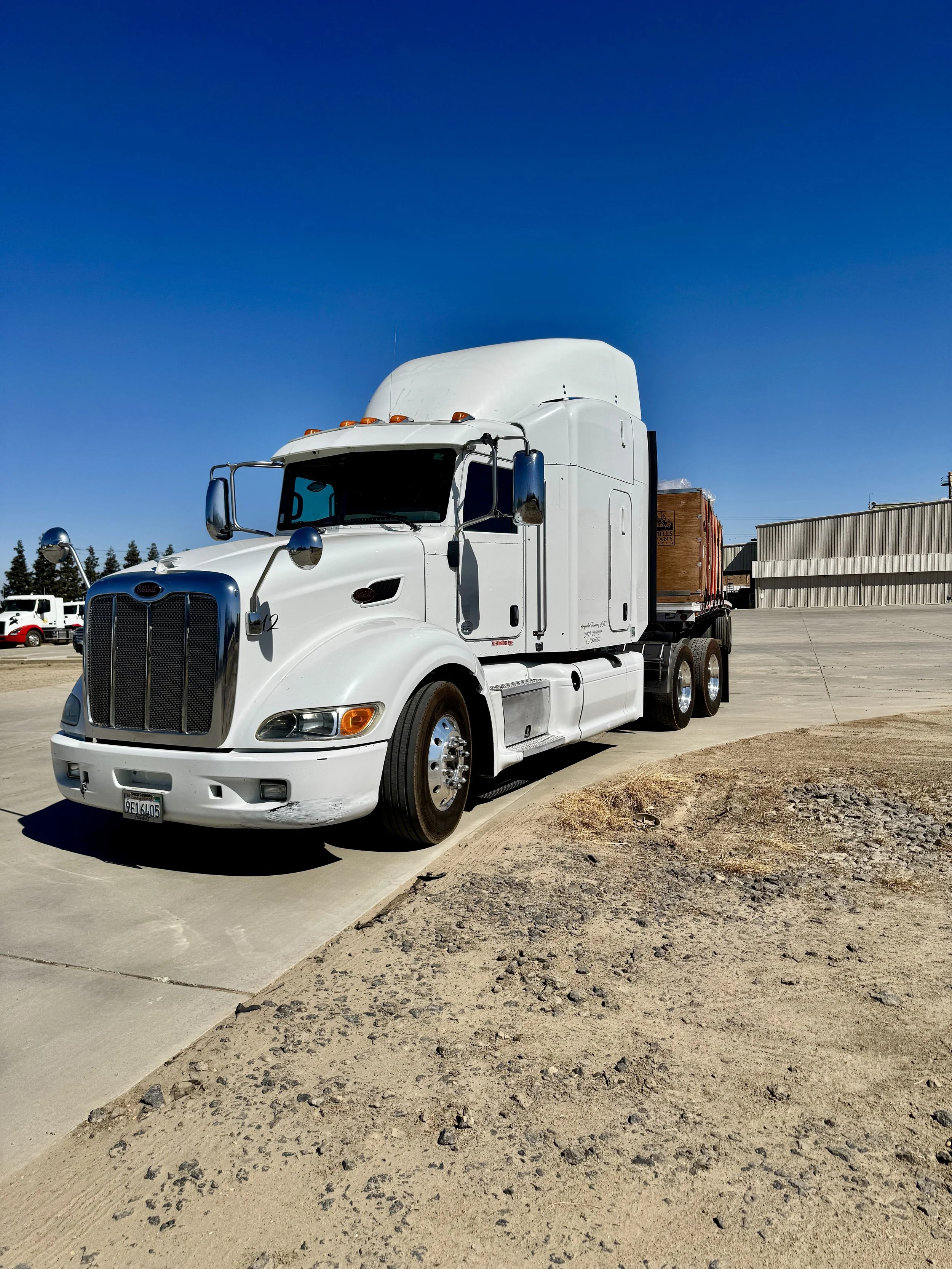 A white semi-truck parked on a concrete lot under a clear blue sky.