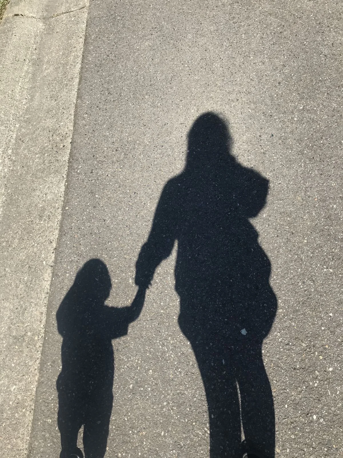 Shadow of an adult holding hands with a small child on a concrete sidewalk in sunlight.