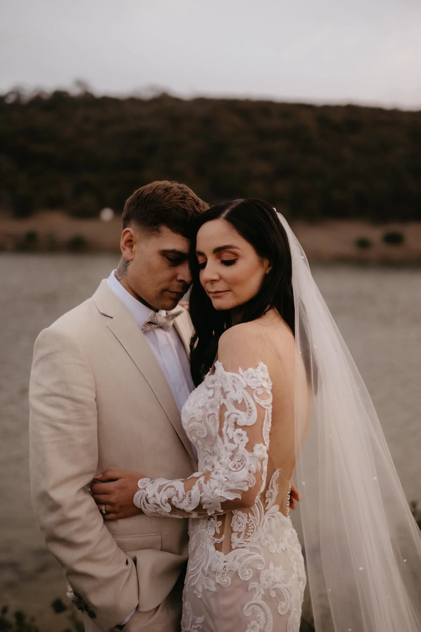 Bride wearing soft bridal makeup with her groom by the water.