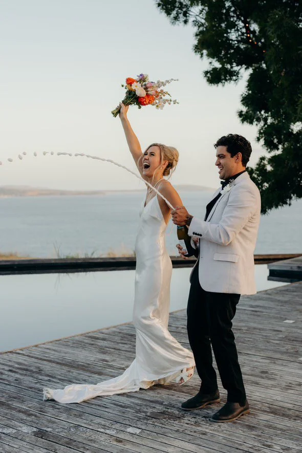 Bride and groom celebrating together by the water on their wedding day.