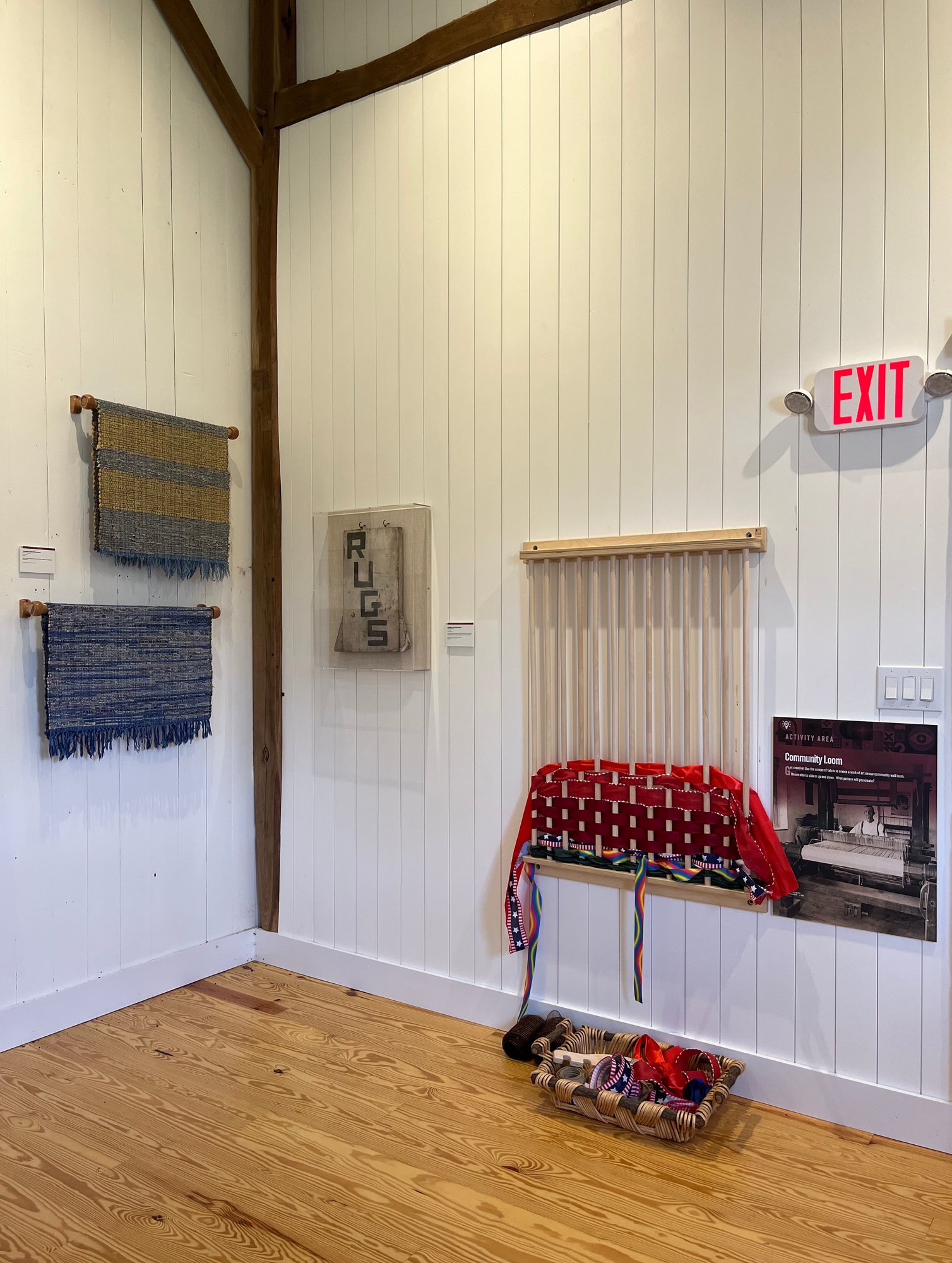 The community wall loom, with woven rugs hanging nearby.