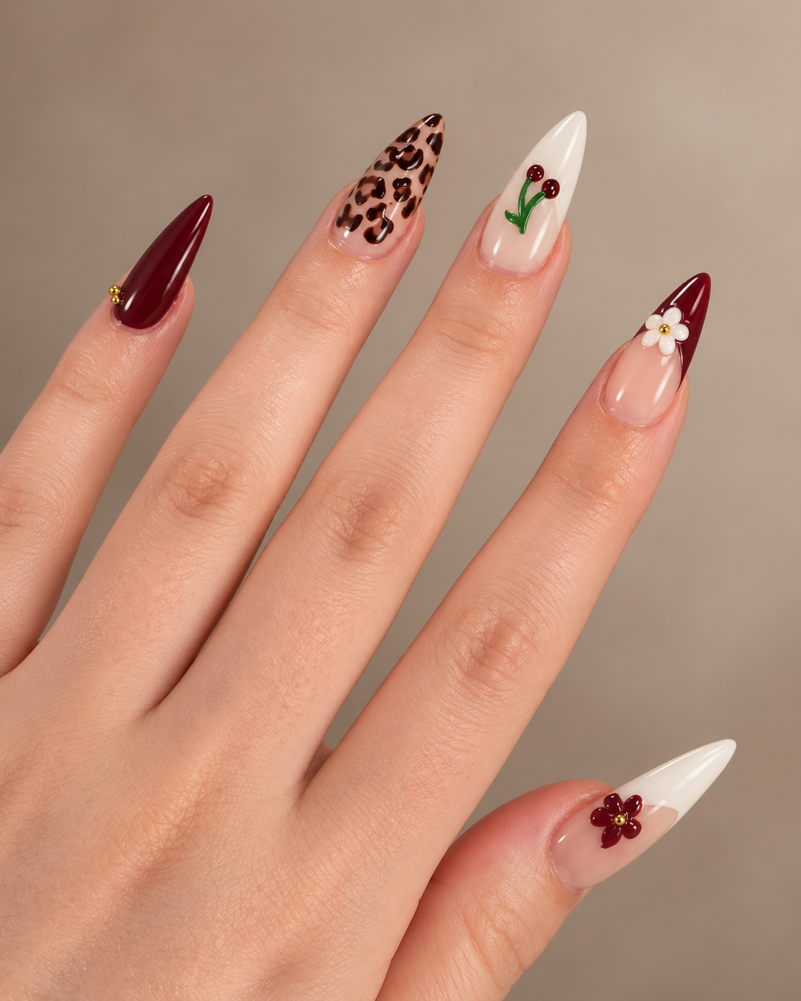 Close-up of a hand with decorated nails featuring various designs including red, leopard print, cherry, and flower patterns.