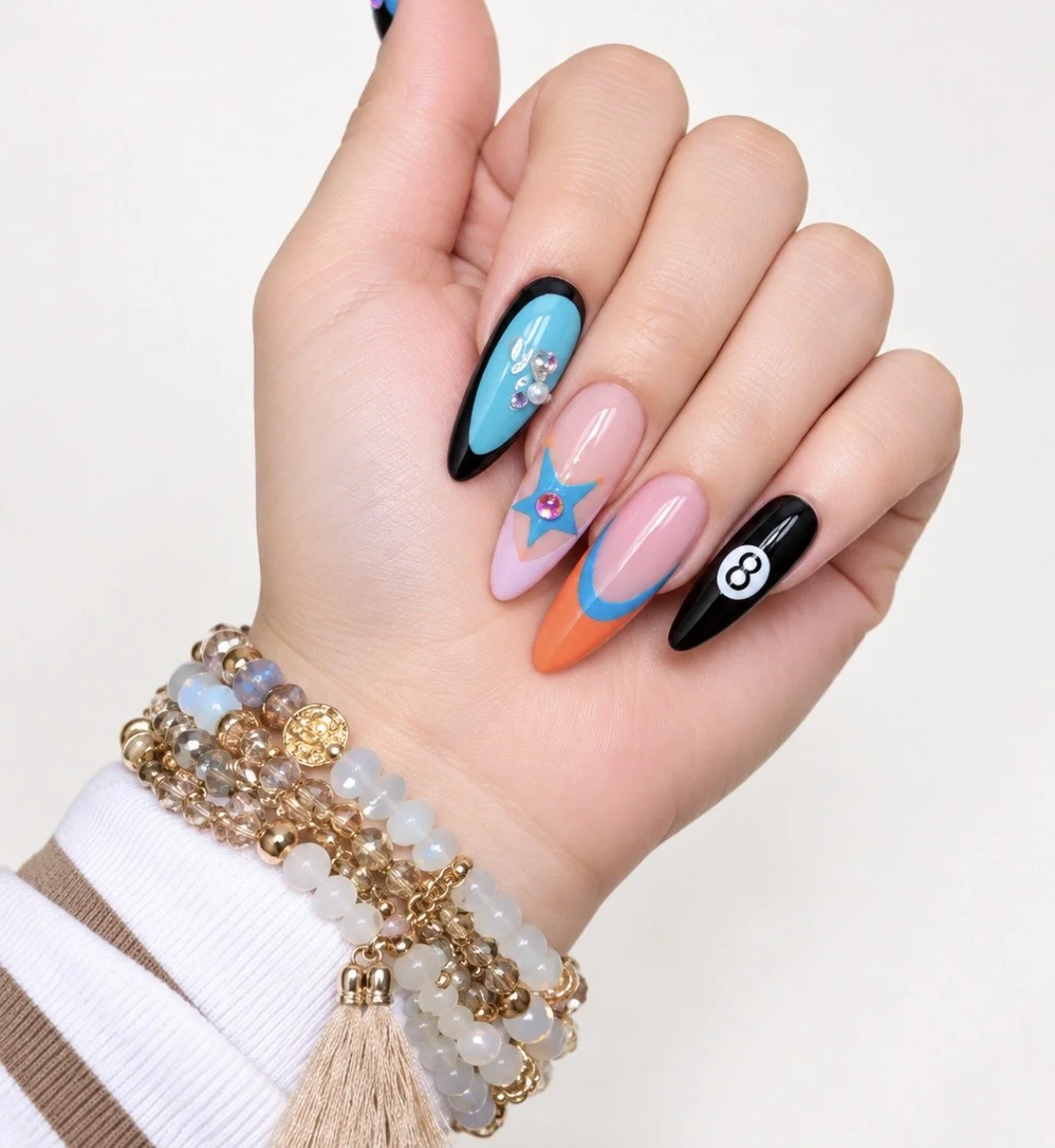 Colorful nail art, featuring black, pink, orange, blue nails with crystals and designs.