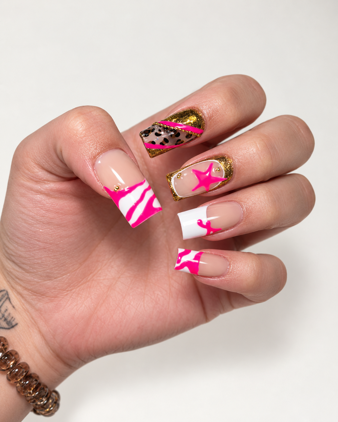 Close-up of a hand with colorful, decorated acrylic nails in pink, white, gold, and leopard print designs.