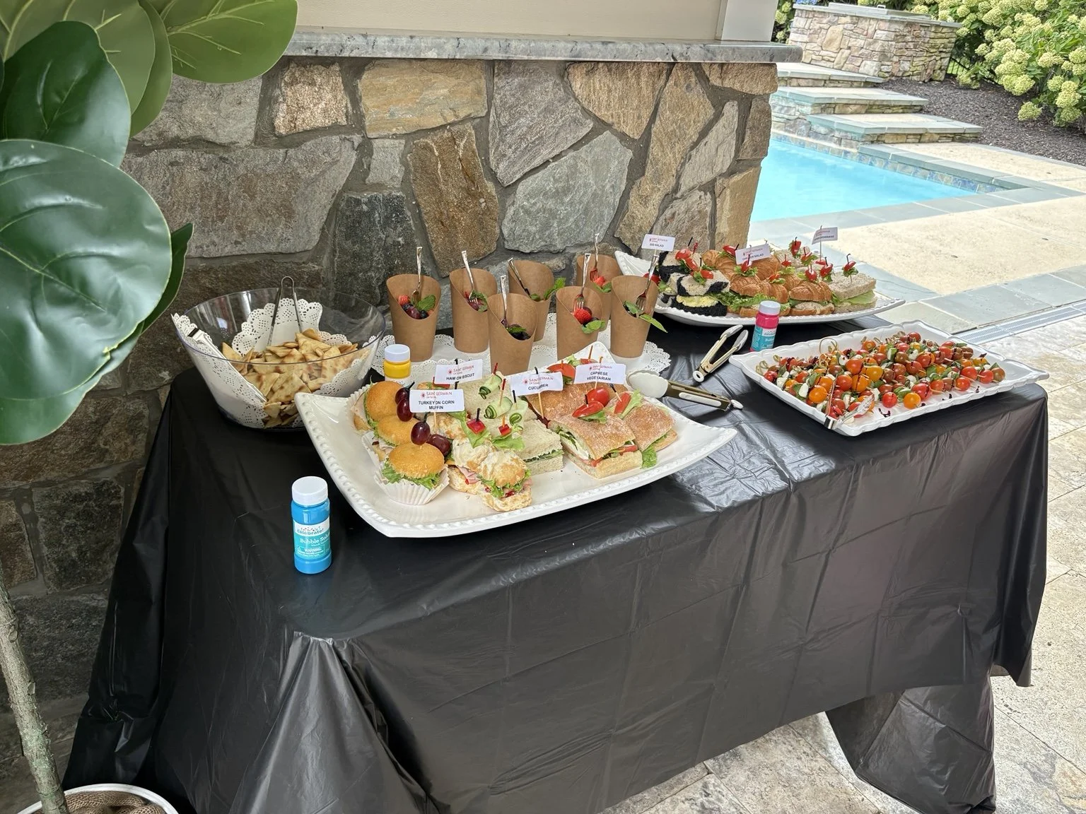 Poolside food spread with tea sandwiches, fruit cups and caprese skewers, thoughtfully arranged for guests.