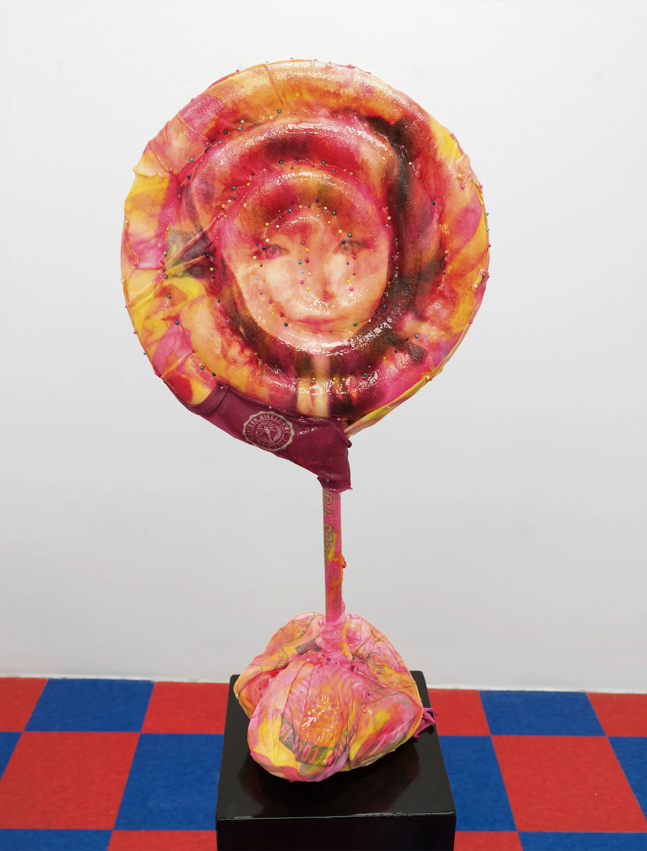 Strawberry (Licker Defeat), 2026. Custom all over print lollipop girl polyester t-shirt size XS, taxidermy pins, plunger, foam, watercolor, acrylic, Abercrombie & Fitch t-shirts, ероху. 12 in. x 35 in. on yellow liquid rubber pedestal.

