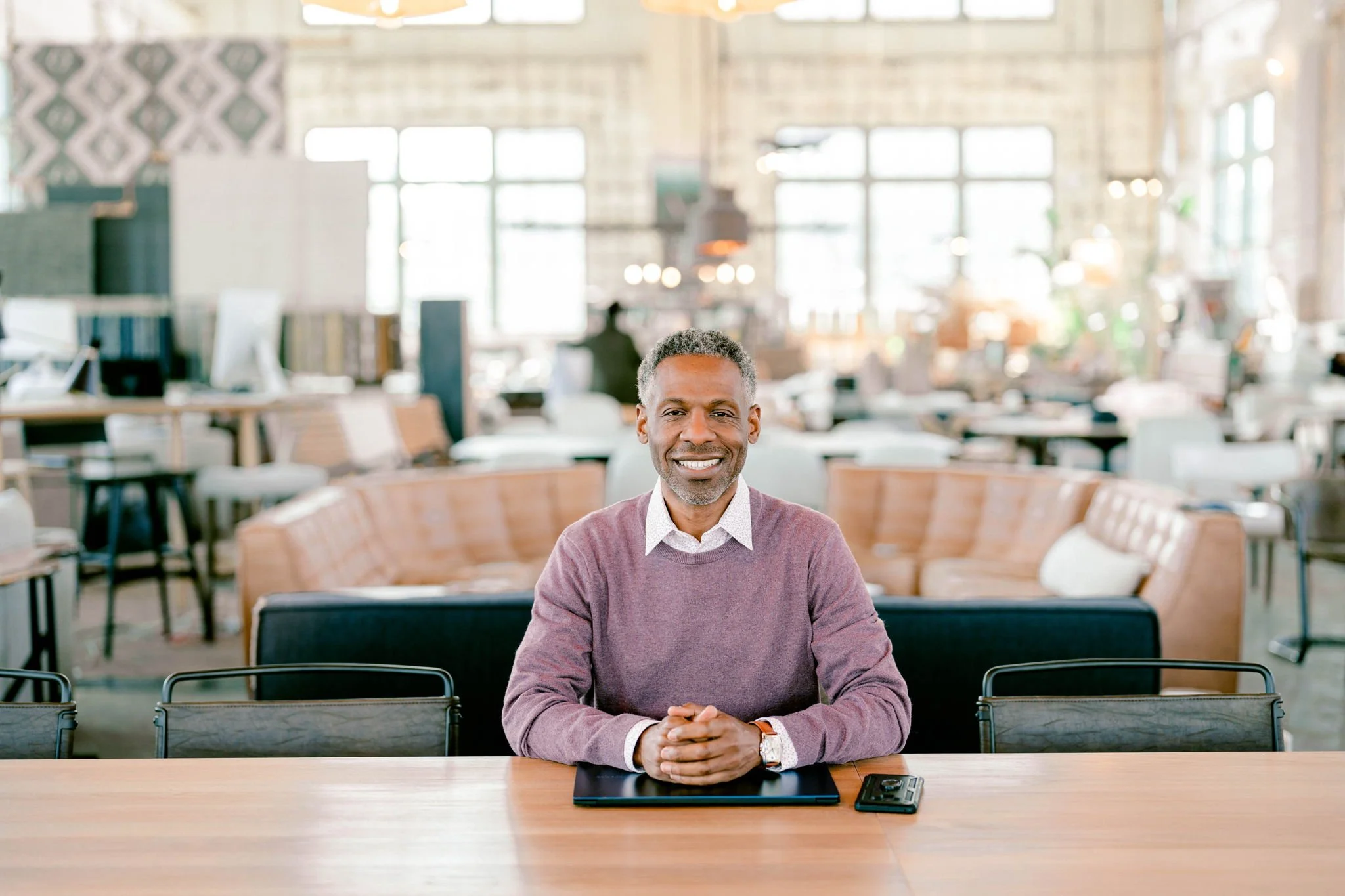 Karloc Paden smiling while seated at a table in a bright, modern interior.