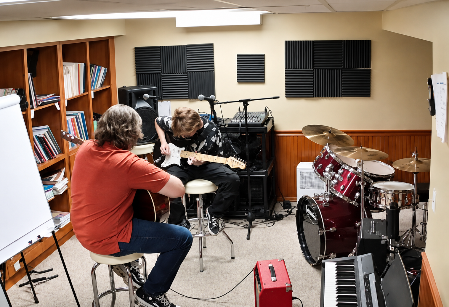 Two people practicing music in a room with musical instruments, bookshelves, and soundproofing panels on the walls.