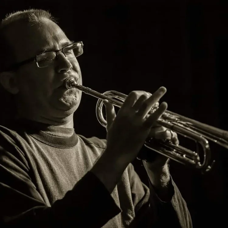 A man wearing glasses playing a trumpet in a dark setting.