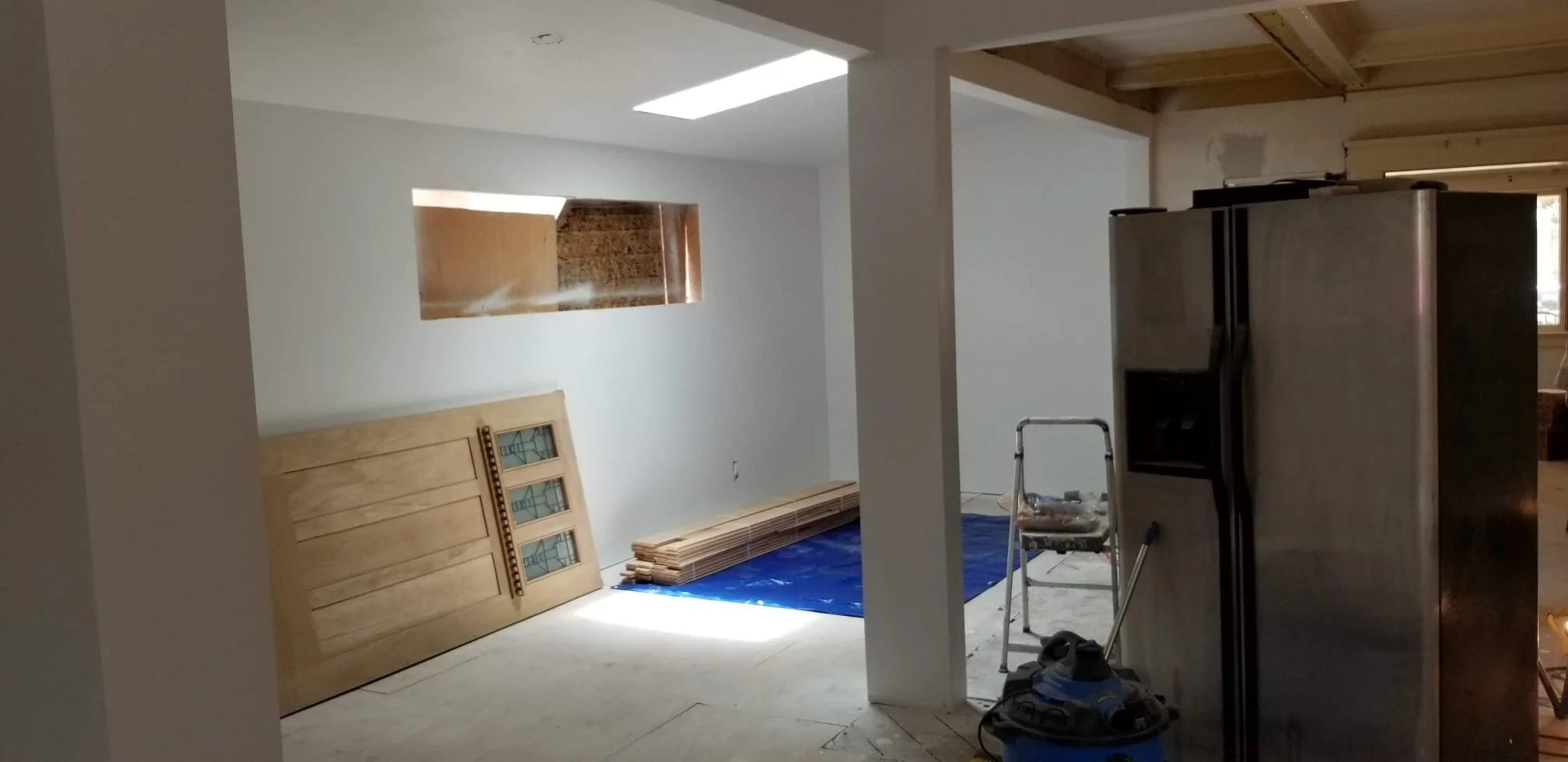 Interior of a room under renovation with construction materials, a ladder, and a refrigerator.