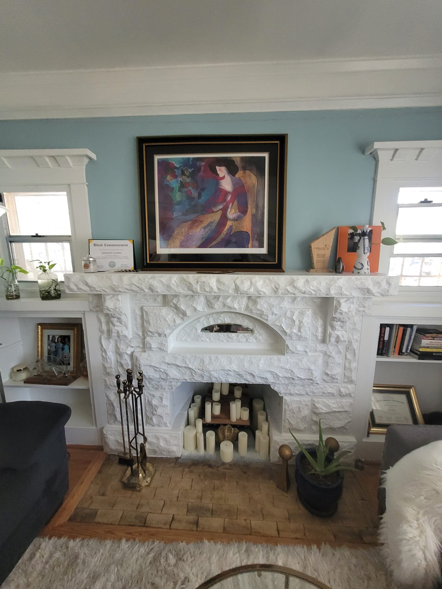 Living room fireplace with decor items, candles, and a framed abstract painting on the wall.