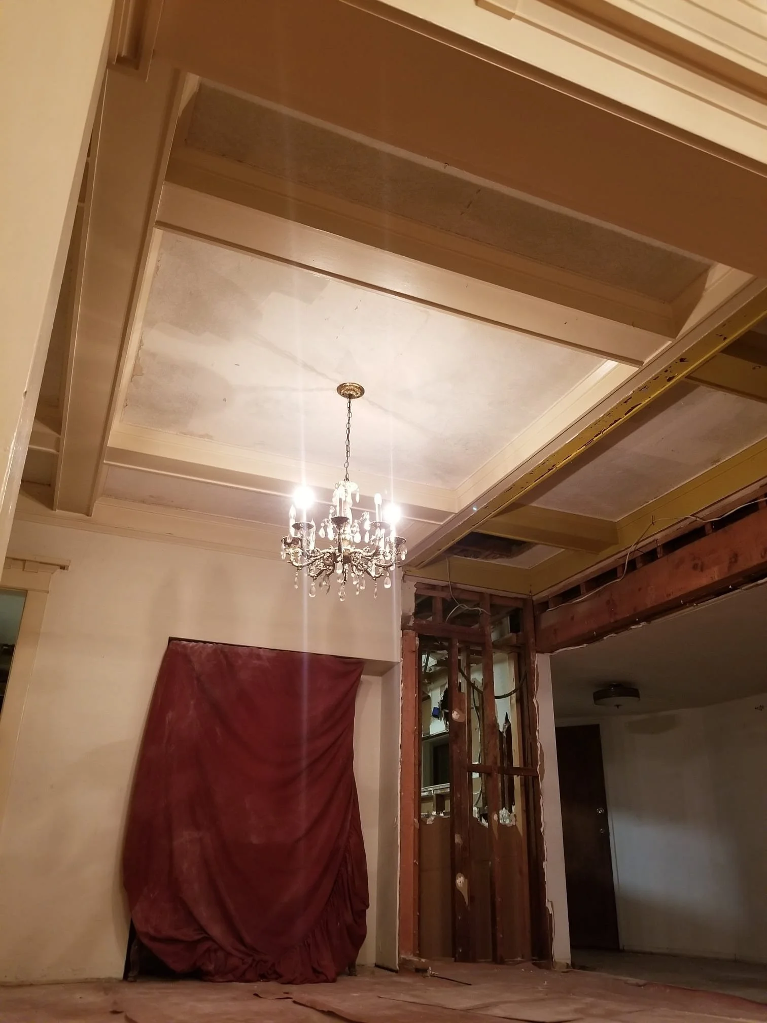 Interior view of a room under renovation, showing drywall and framing work in progress, with a chandelier hanging from the ceiling.