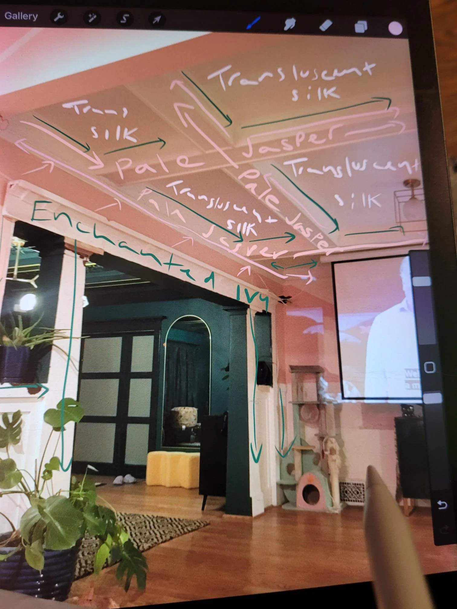 A room interior with a ceiling painted pink and featuring handwritten notes and arrows in various colors, including words like 'Translucent', 'Silk', 'Pale', and 'Jasper'. There are plants, a black door with a window, a colorful rug, a yellow ottoman