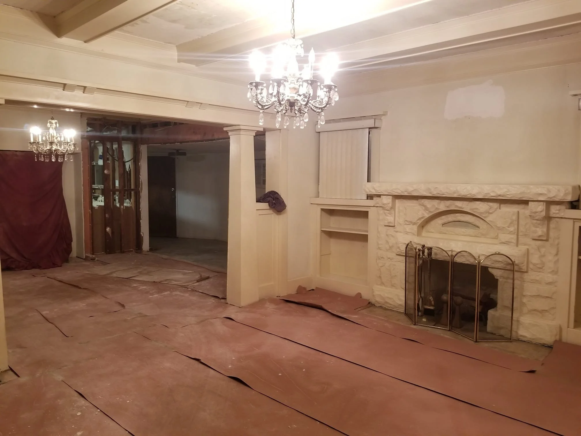 Living room with stone fireplace, chandelier, and partially finished ceiling and flooring during renovation or construction.