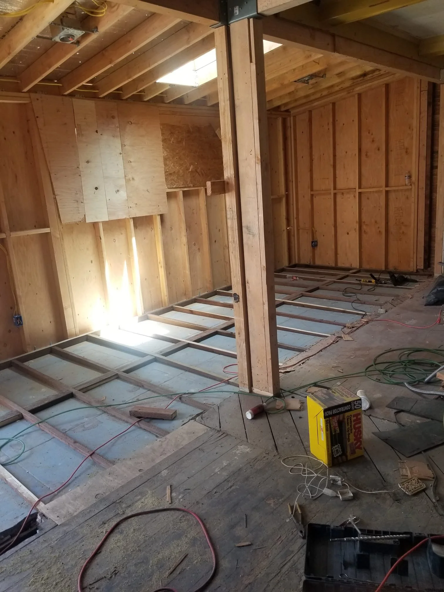 Construction site with exposed wooden framing and electrical wiring, partially built interior walls, and various tools and materials on the floor.