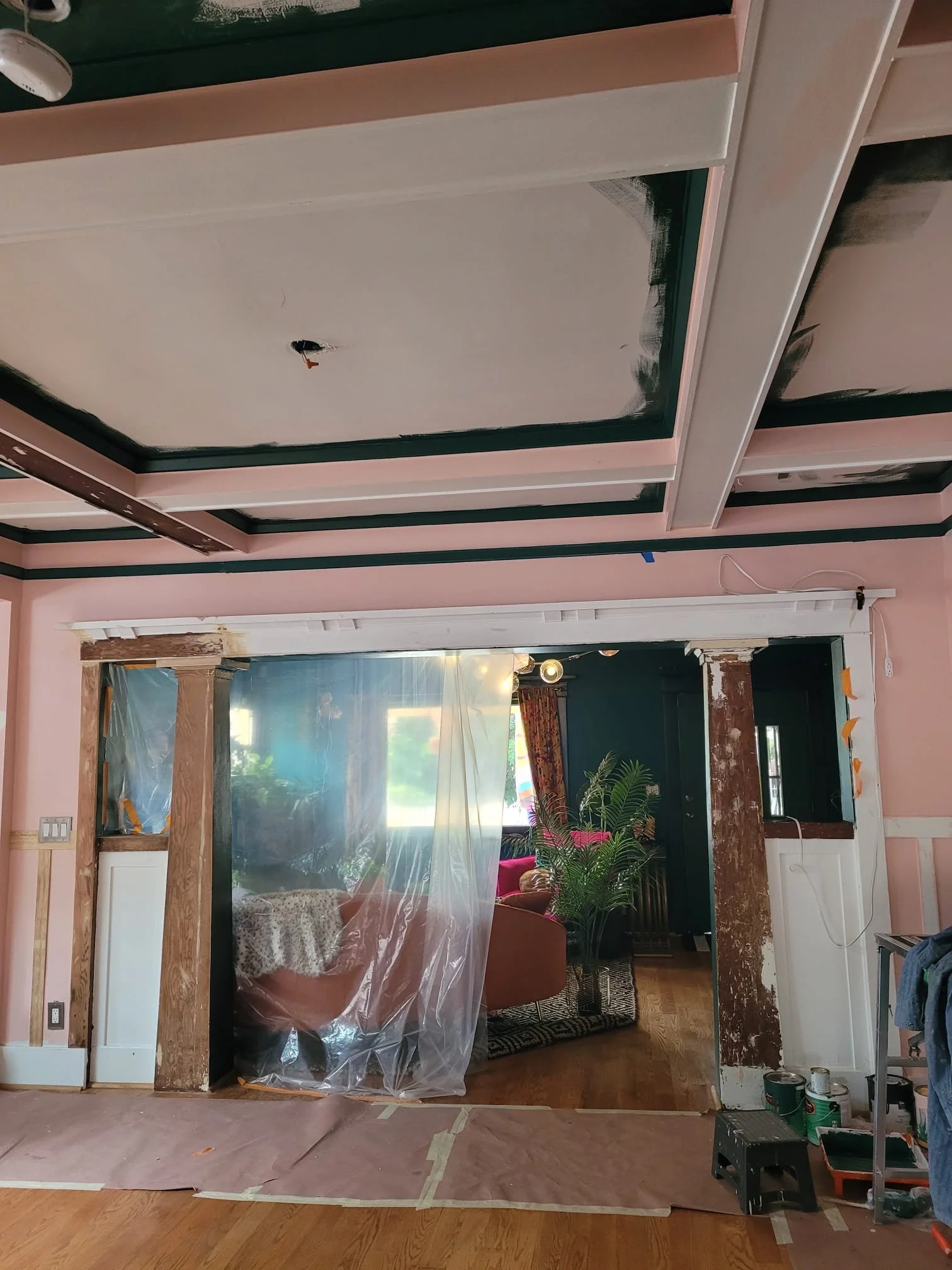 Interior of a room under renovation with a large mirror or glass panel, partially covered with plastic; construction tools and supplies are visible, with wooden beams and walls being worked on.