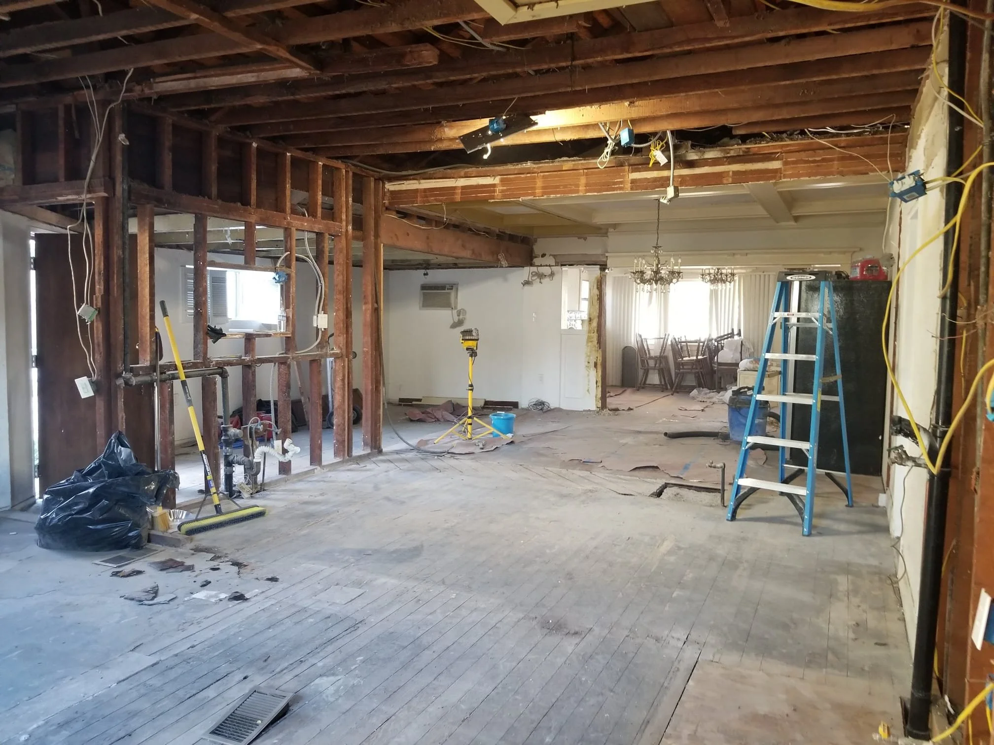 Interior view of a house undergoing renovation, showing exposed wooden framing, construction tools, and partially removed drywall.