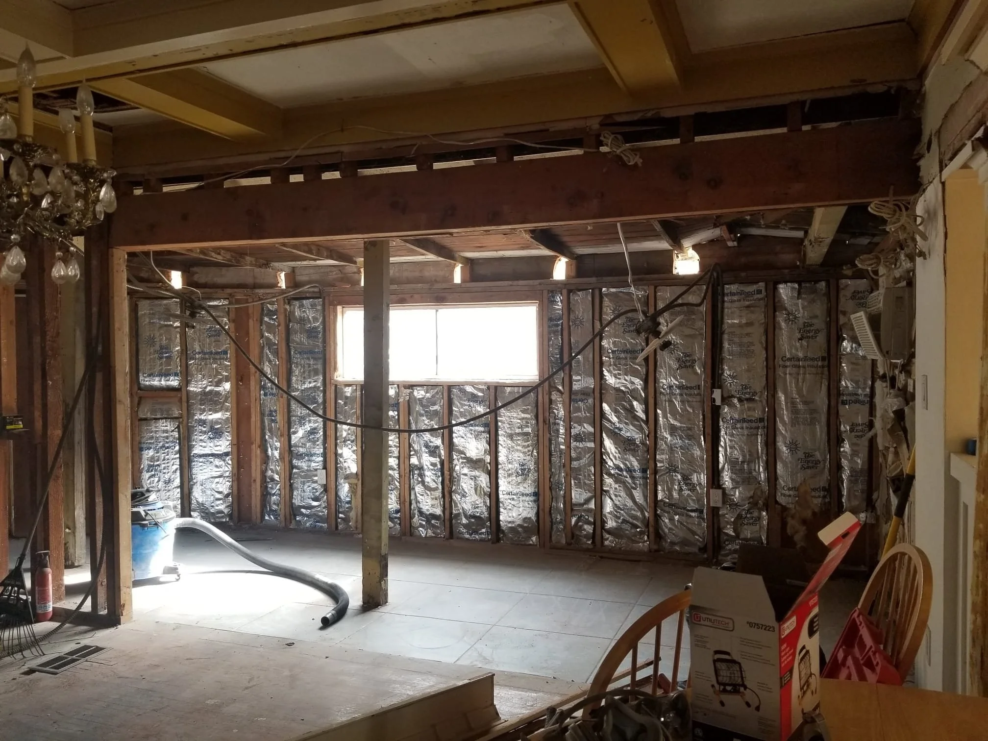 A room under renovation with exposed wooden framing, insulation, and construction tools and material scattered around.