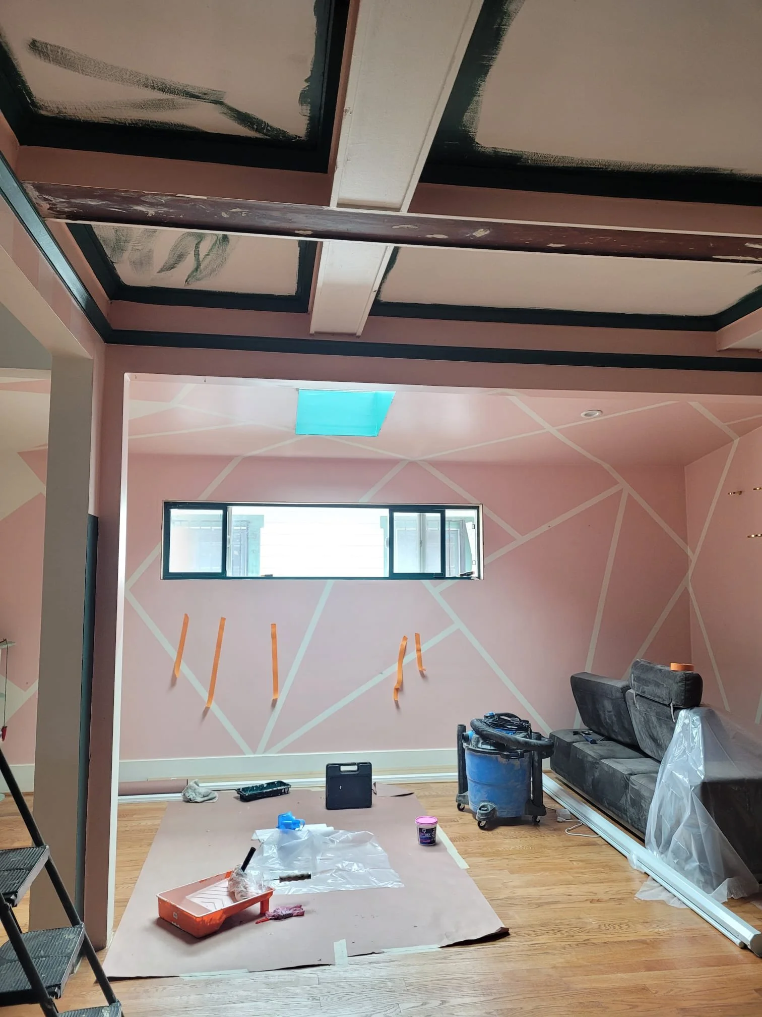 Room undergoing renovations with tools, paint supplies, and partially painted walls with geometric pattern.