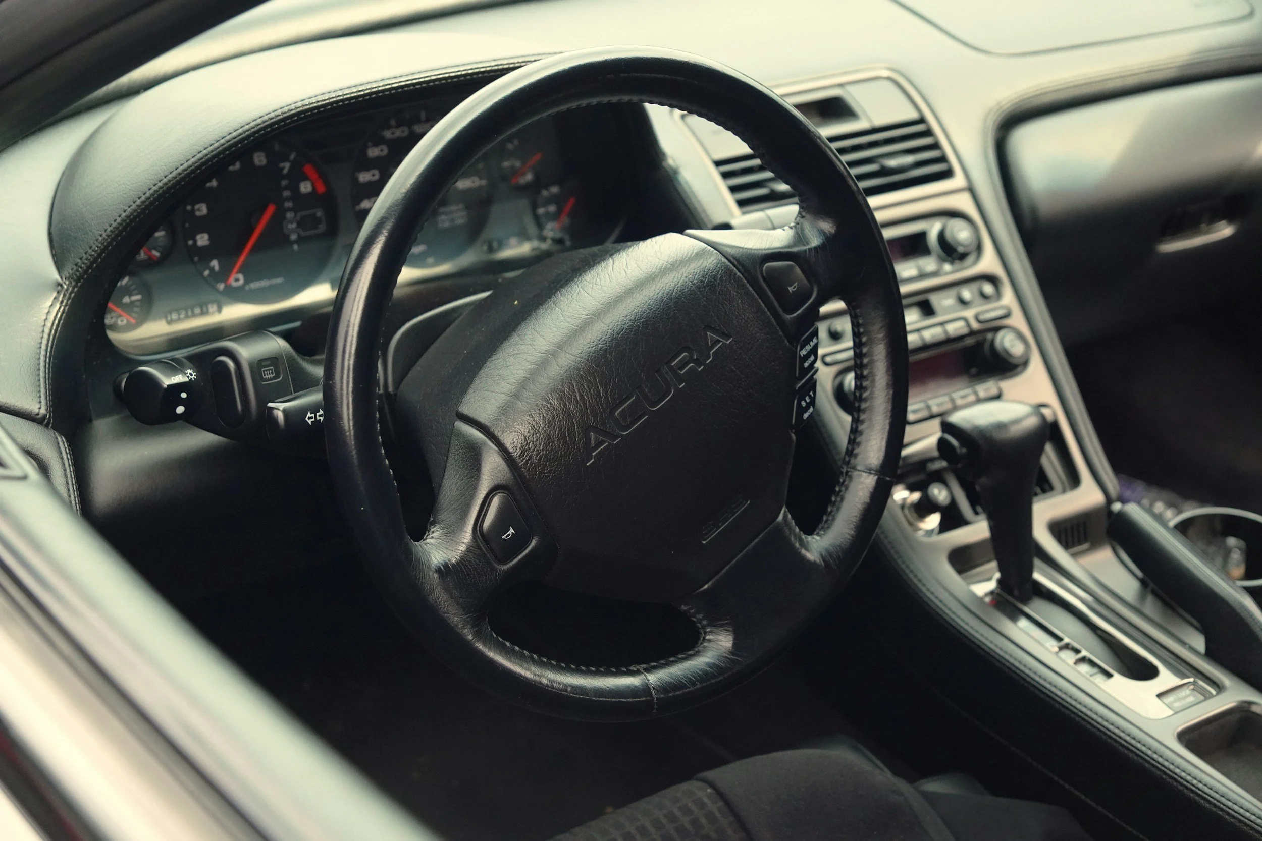 Interior of a car showing steering wheel with 'ACURA' logo, dashboard, and center console with gear shift.