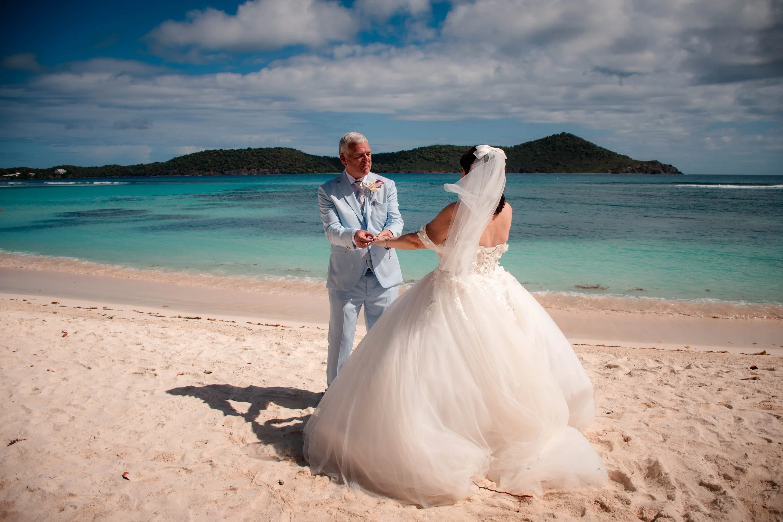 A bride and groom exchanging vows on a beach with turquoise water and green islands in the background.