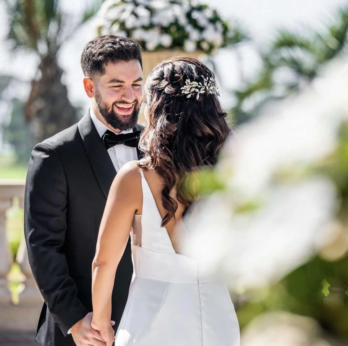 Bride and groom exchanging vows outdoors during their wedding ceremony, holding hands and smiling at each other.