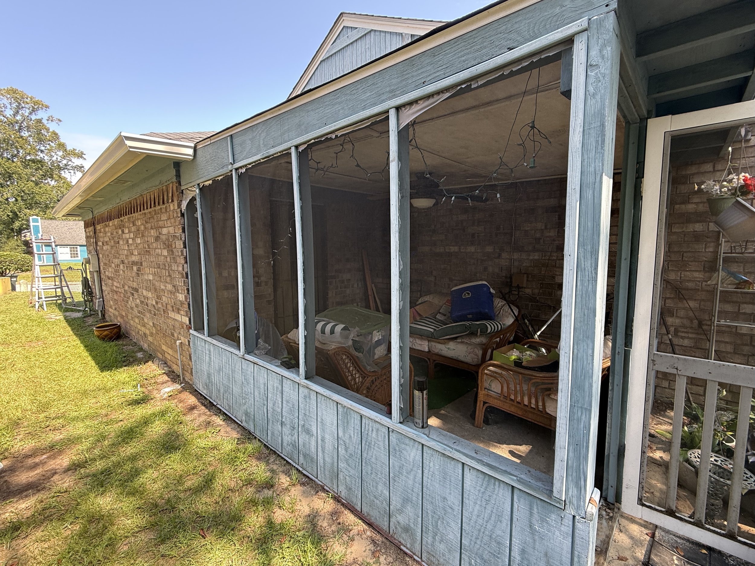 Back porch of a house with a brick wall, a screened-in section with furniture and string lights, and a ladder in the yard.