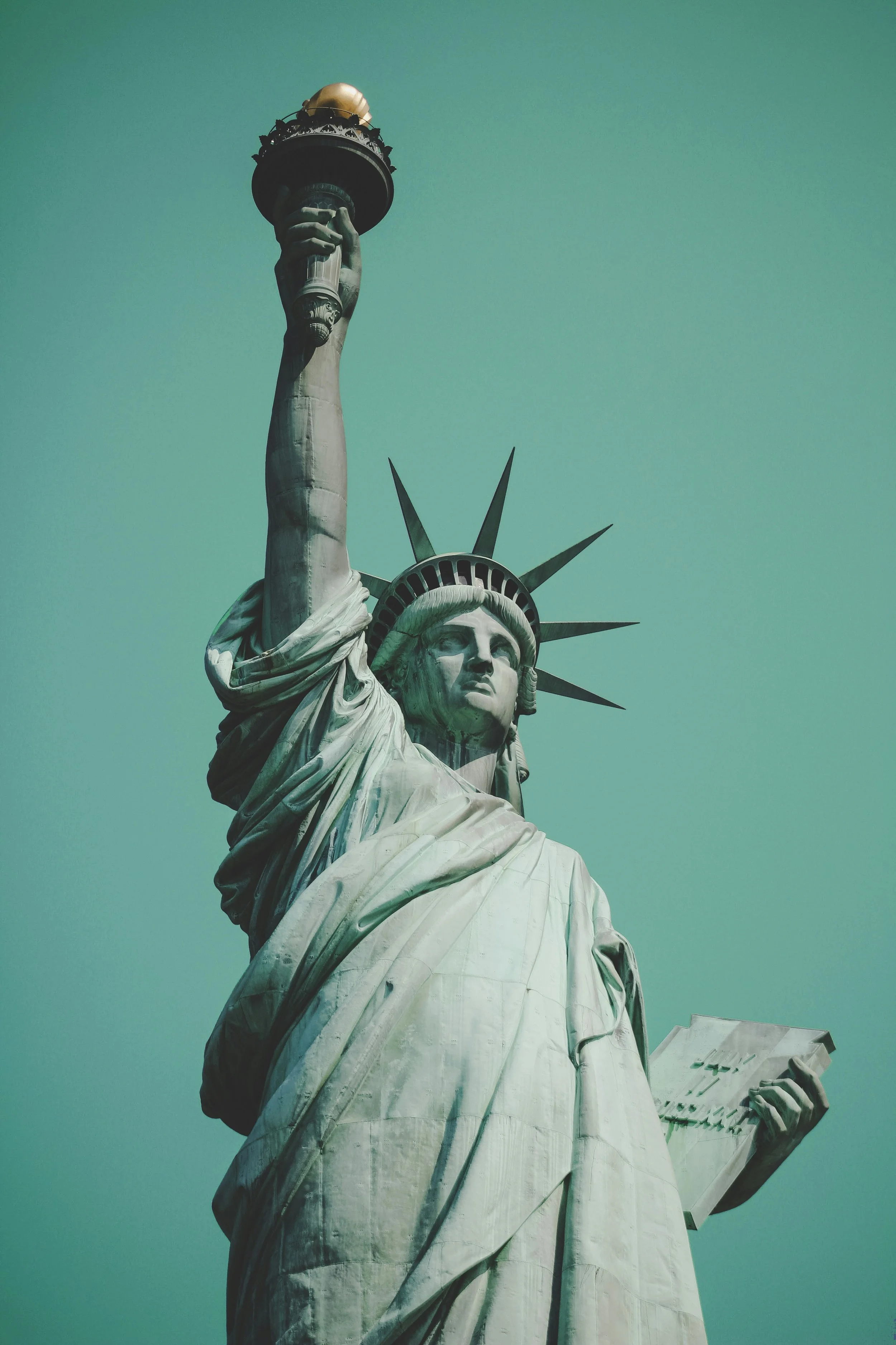 Close-up of the Statue of Liberty's face, torch, crown, and part of her robe against a clear sky.