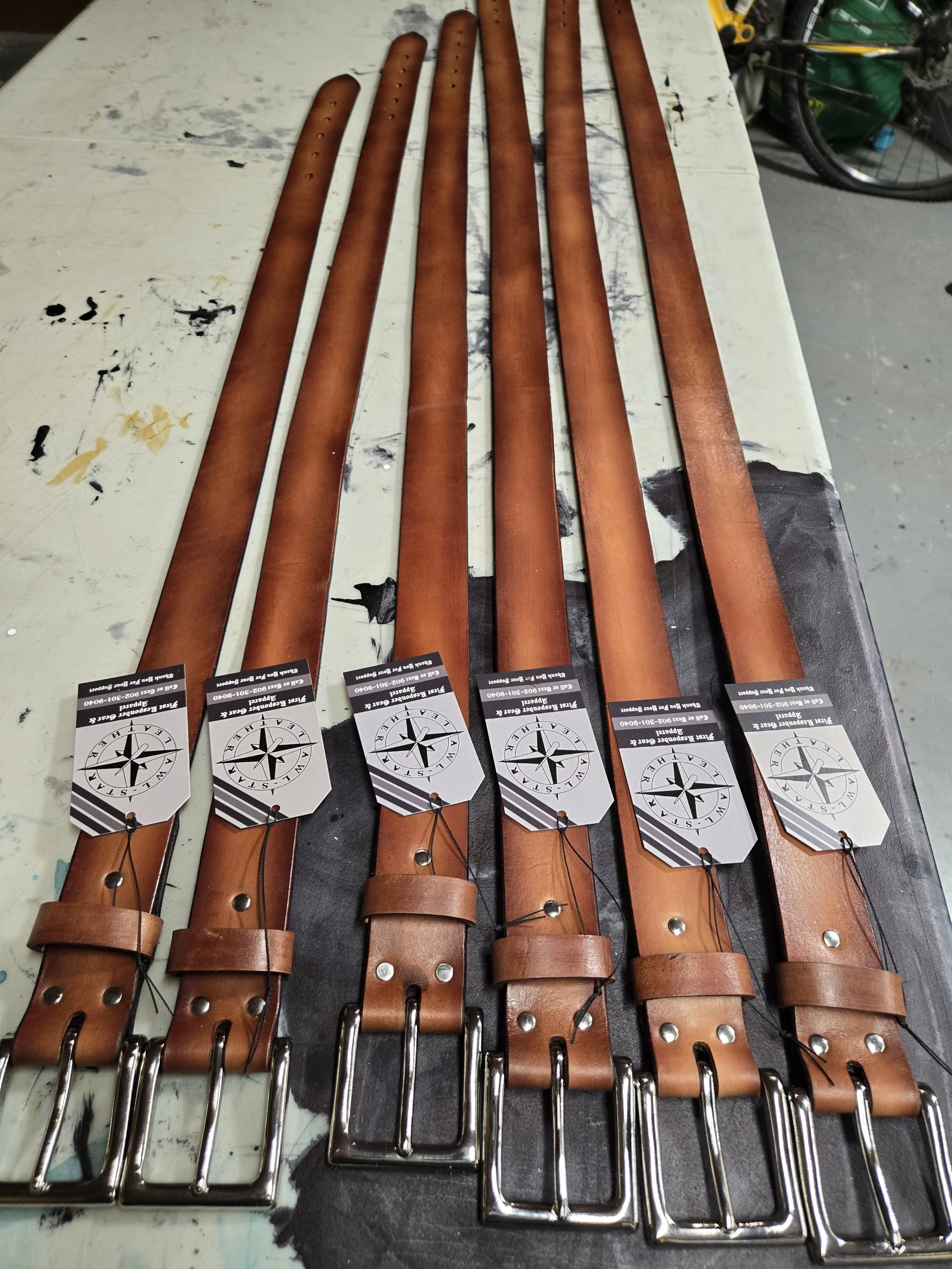 Six handcrafted Awl Star Leather single ply belts laid out on the workbench during production.