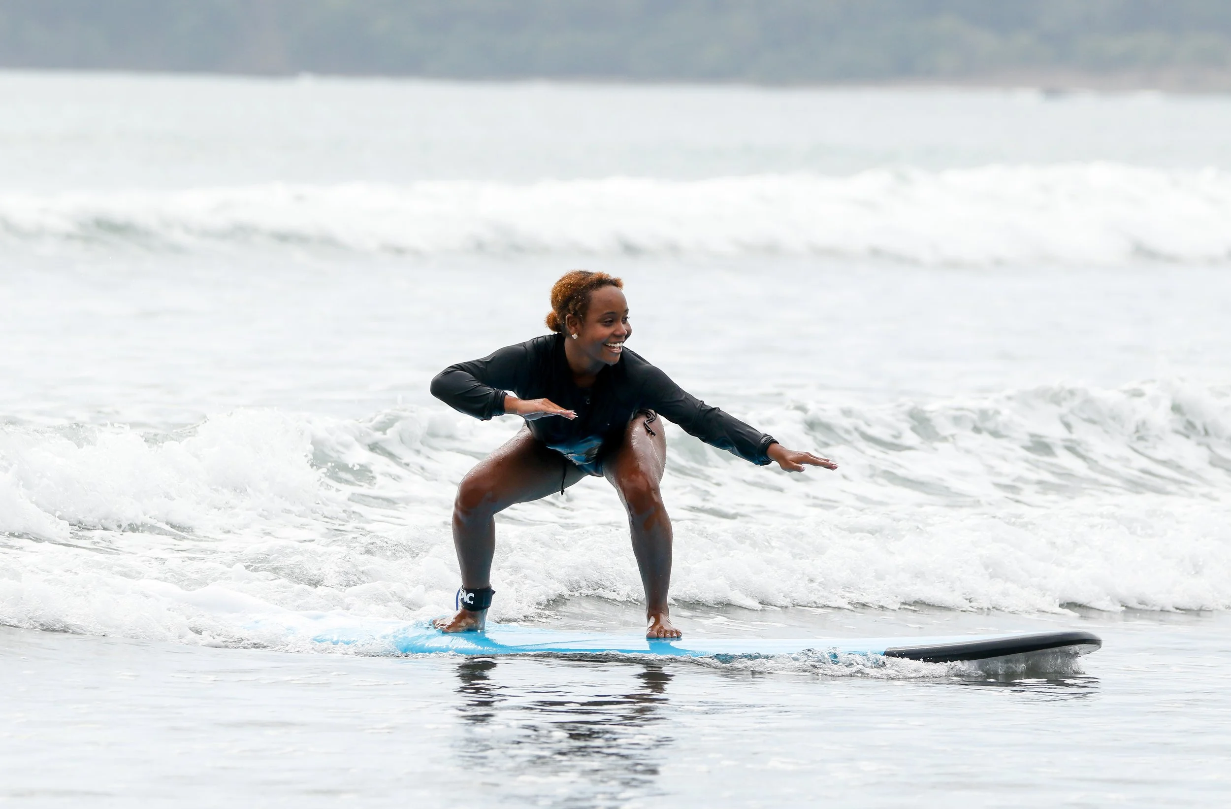 A woman smiling and crouching on a surfboard in the ocean, preparing to ride a wave.