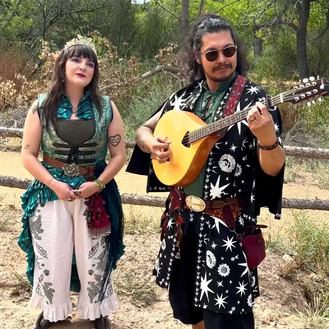Secret Moss Meadow band members performing outdoors in Celtic fantasy garb, with Emily singing and Eric playing the Irish bouzouki.