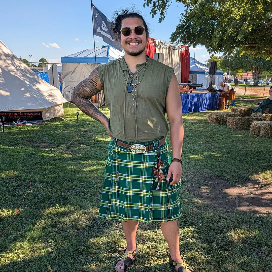 Eric, multi-instrumentalist for Irish folk duo Secret Moss Meadow, wearing a green tartan kilt and sunglasses at an outdoor festival.