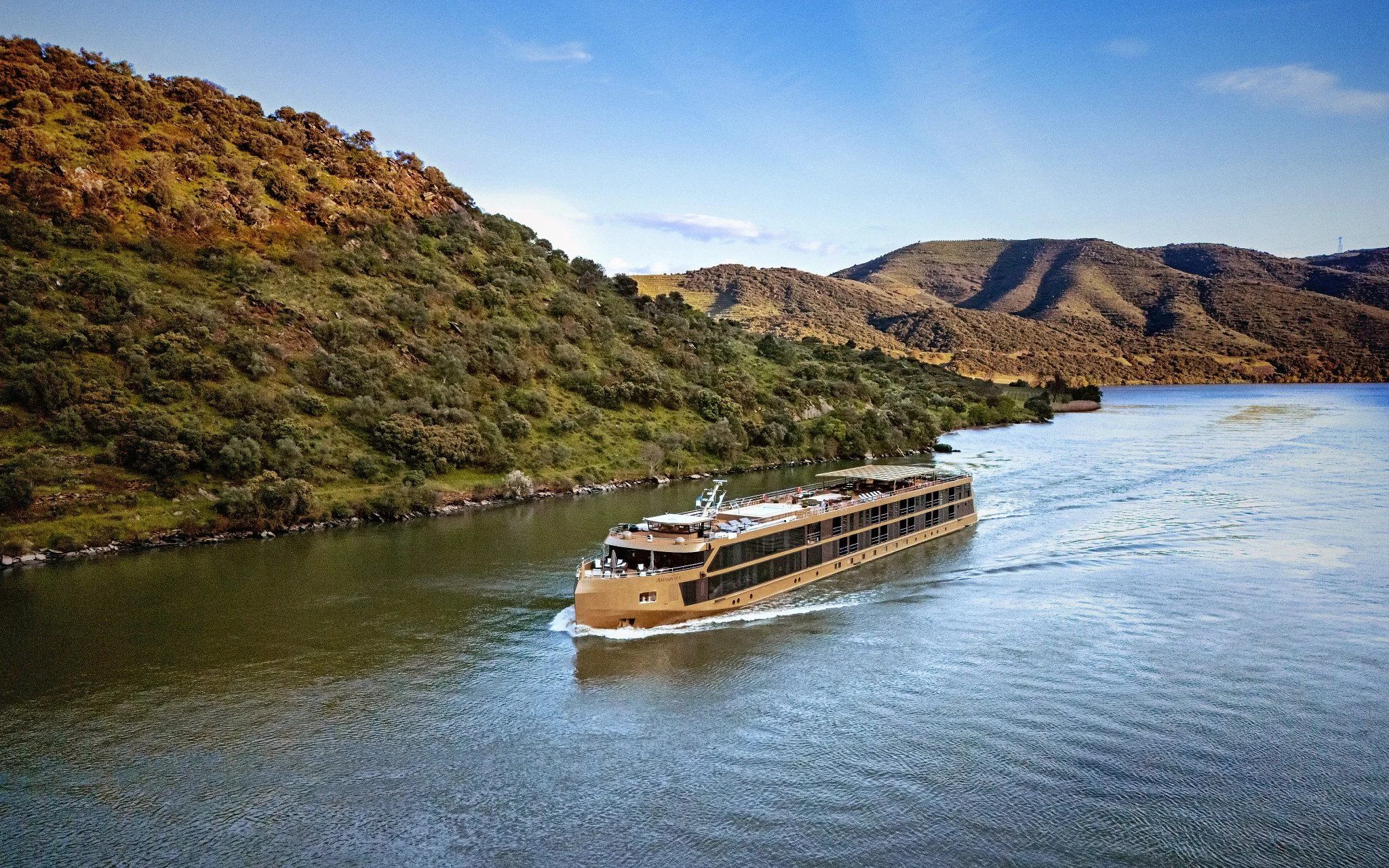 River cruise ship sailing through a scenic European river valley.