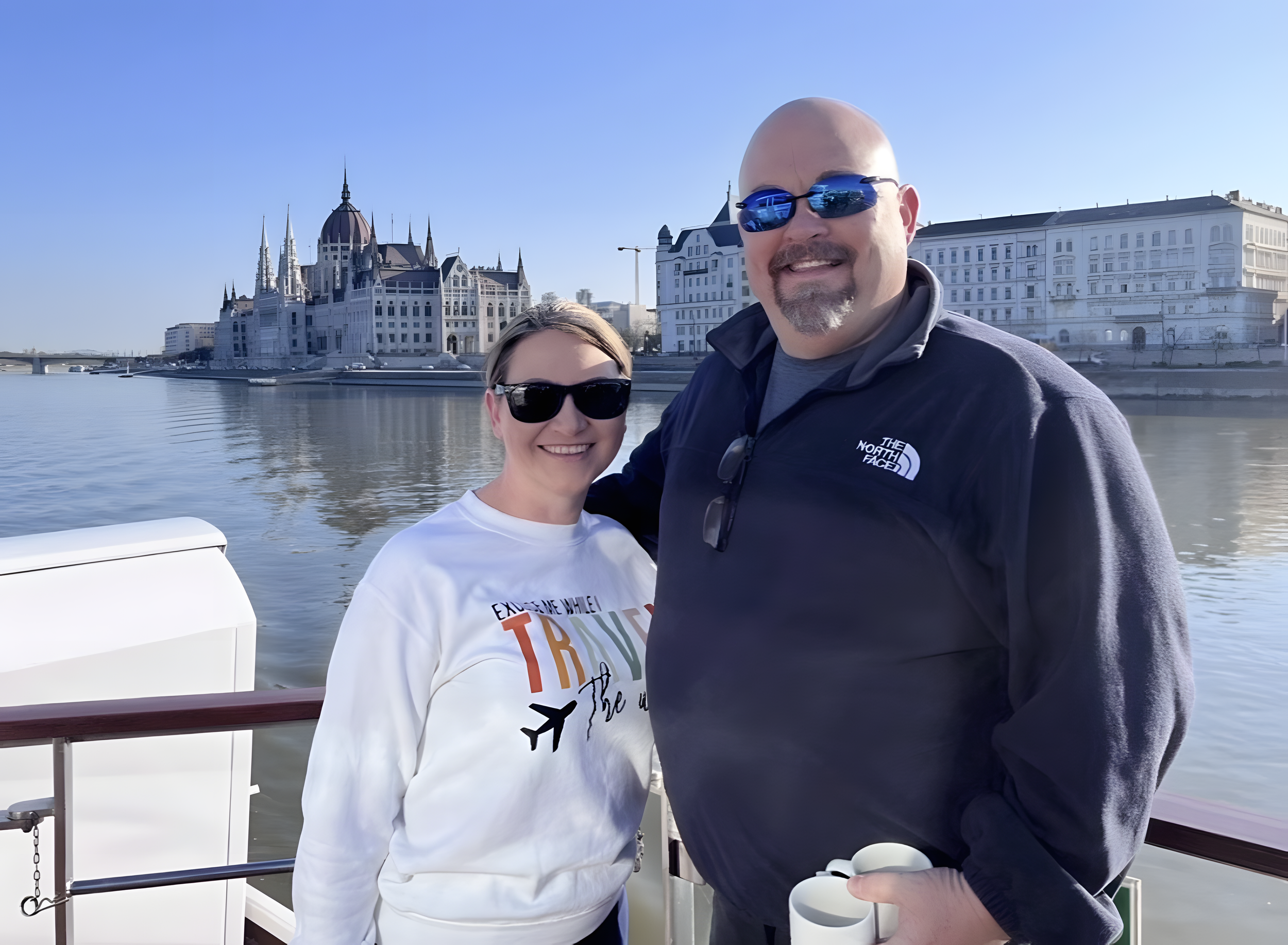 Couple enjoying a river cruise with a European city in the background.