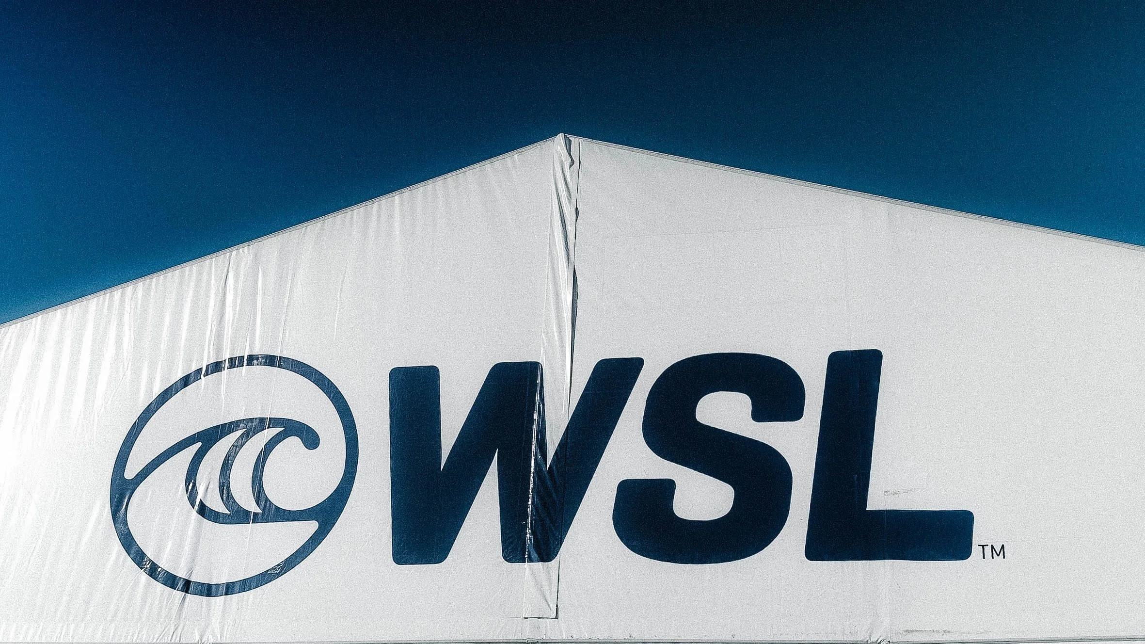 Close-up of a white object with the partial word 'WASTE' and a circular logo, against a clear blue sky.