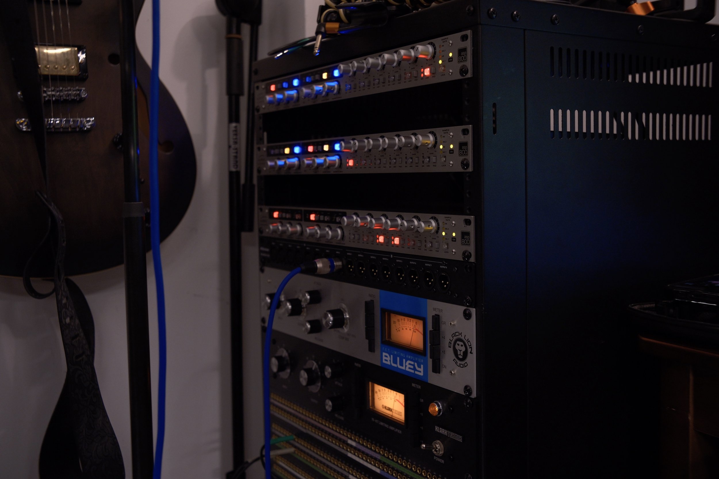 A rack of audio equipment including various amplifiers, equalizers, and audio processors with illuminated controls and meters.