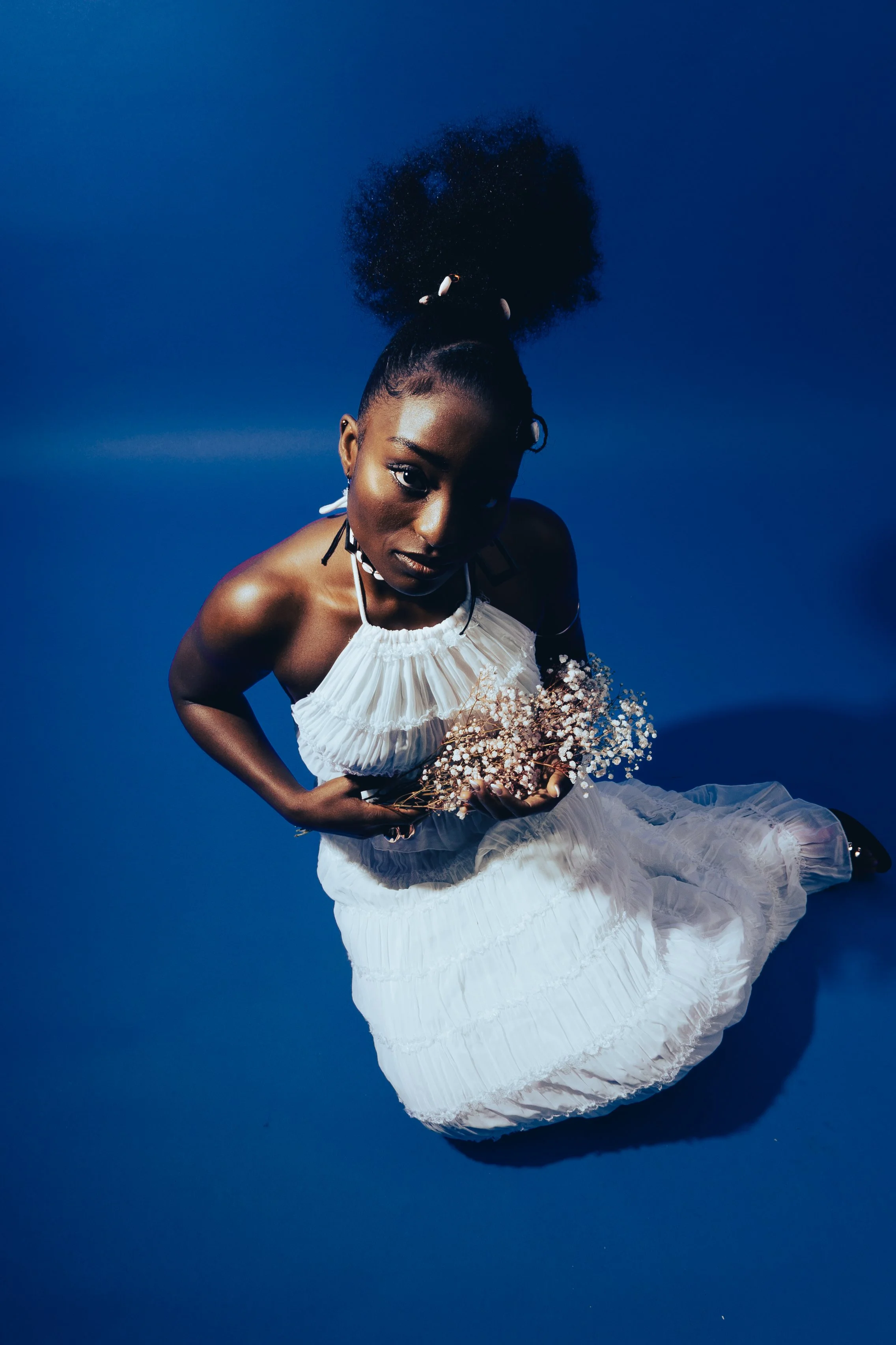 Frau in Weißes Kleid mit weißen Blumen, im Wasser gegen blauen Himmel, trägt Afro-Haar mit schwarzem Haarkamm, hält einen Blumenstrauß.