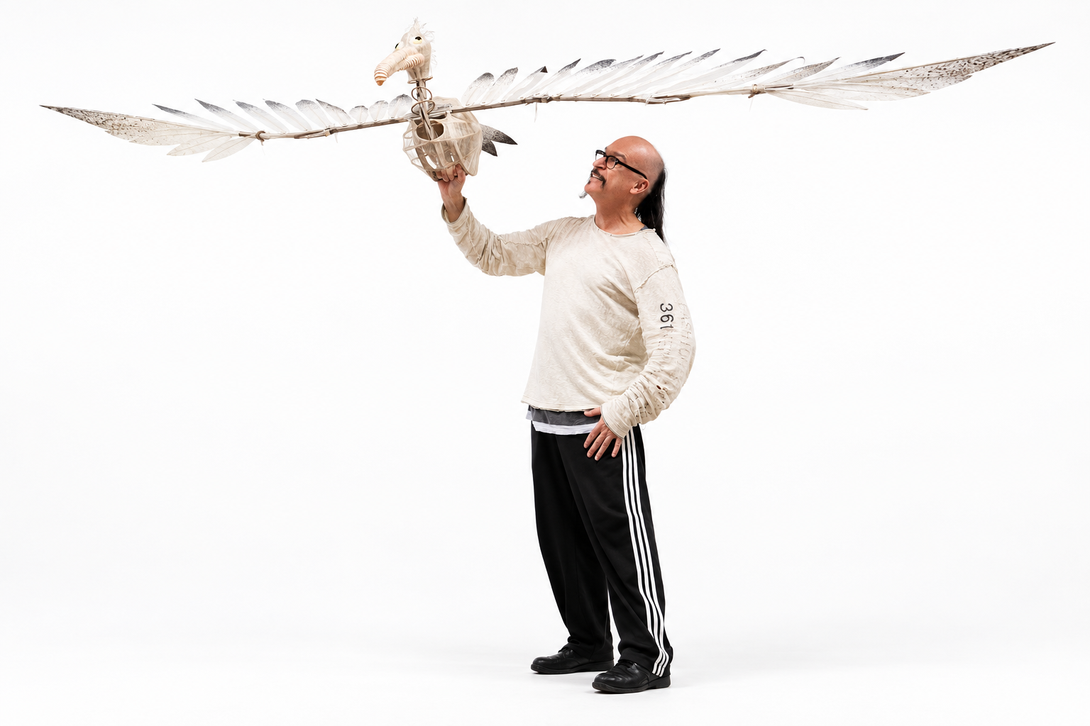 Peter Wilson wearing a long-sleeve shirt and black track pants, holds a large, decorative, stylized bird puppet with wings spread wide.