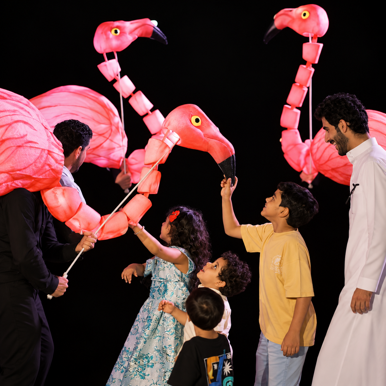 People, including children, are celebrating with large pink flamingo-shaped lanterns.