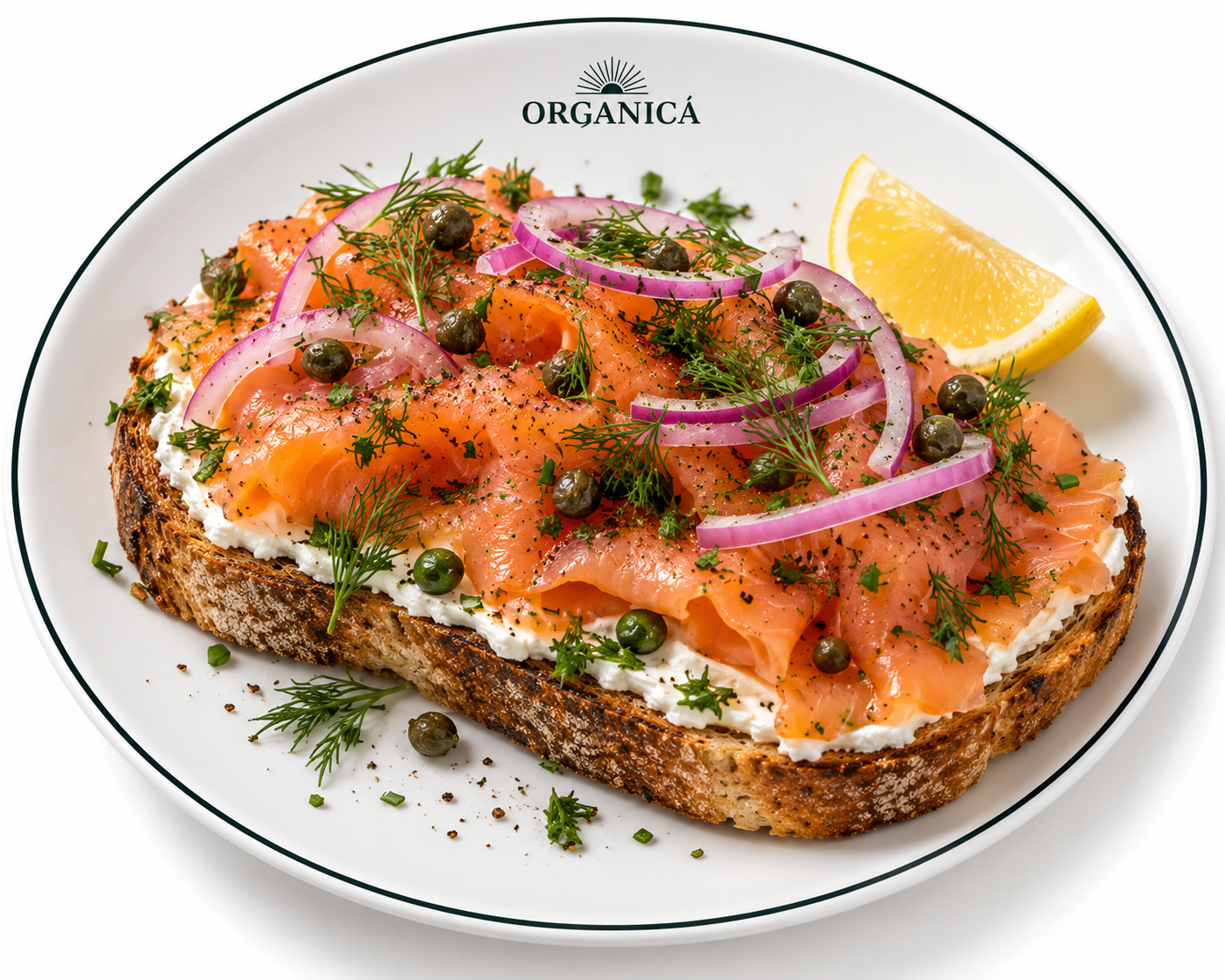 Open-faced smoked salmon sandwich on toasted bread with cream cheese, red onion, capers, dill, black pepper, and a lemon wedge on a white plate.