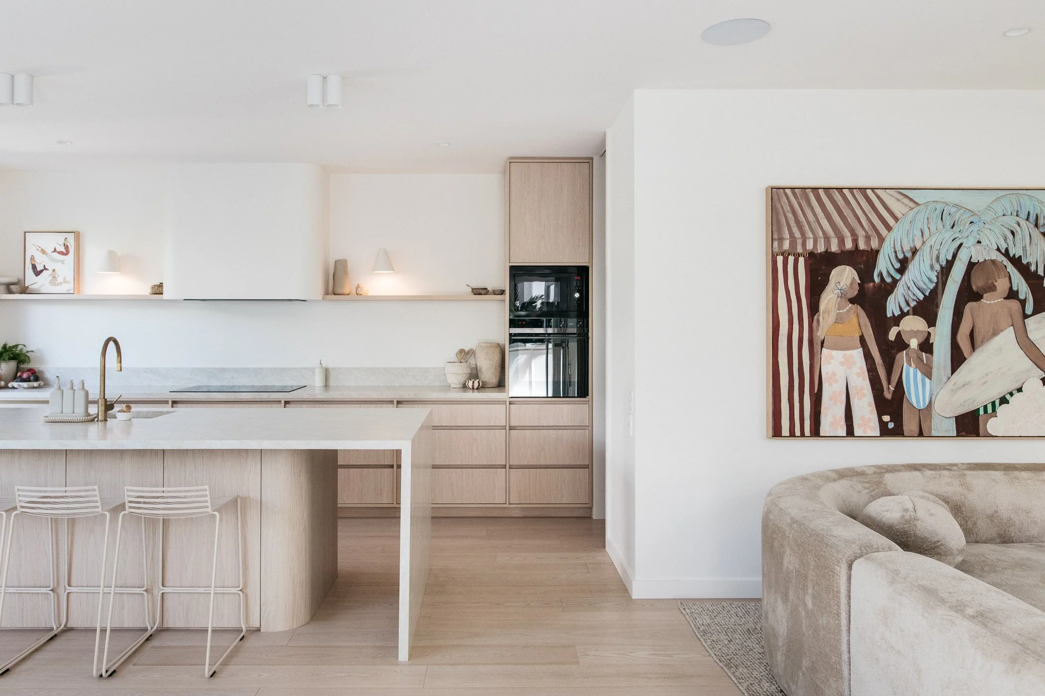 Modern kitchen with white island, light wood cabinetry, built-in oven, and colorful artwork on the wall.